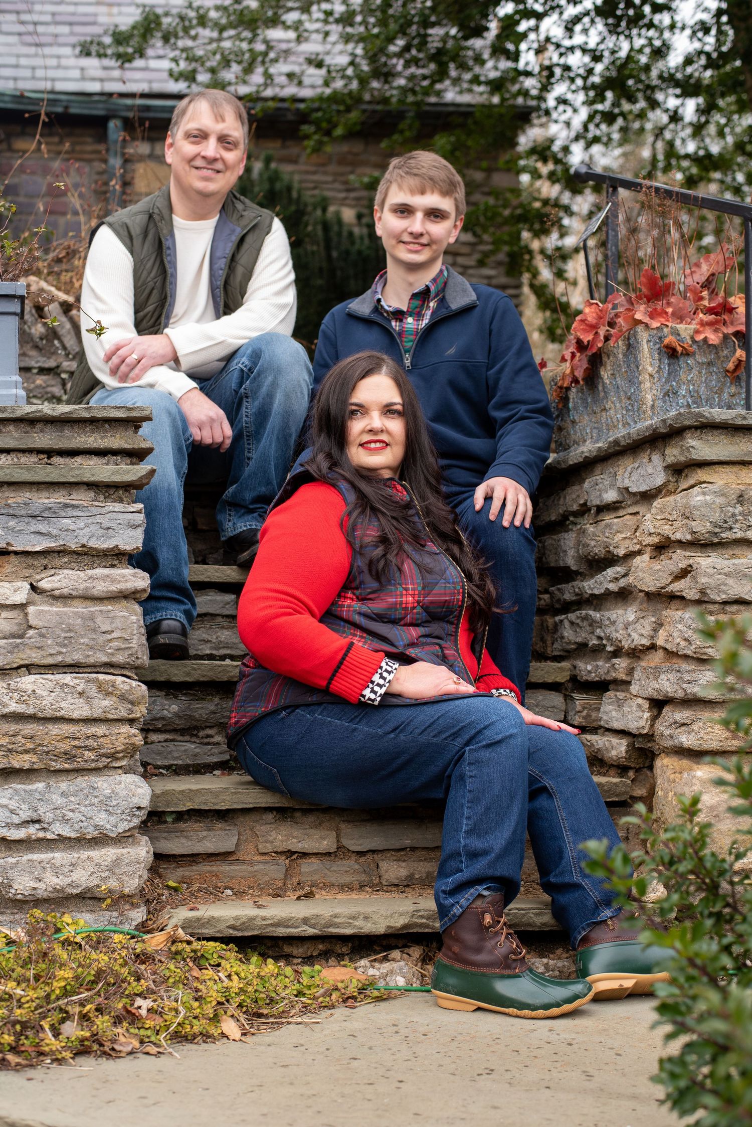 Family of three poses on stone steps surrounded by autumn foliage during an outdoor family portrait session.
