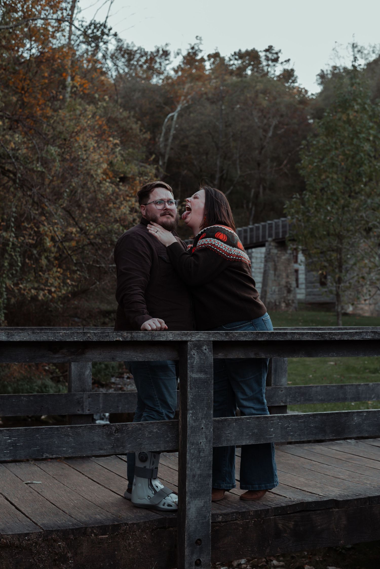 Couple sharing a romantic moment on a rustic wooden bridge surrounded by autumn foliage.