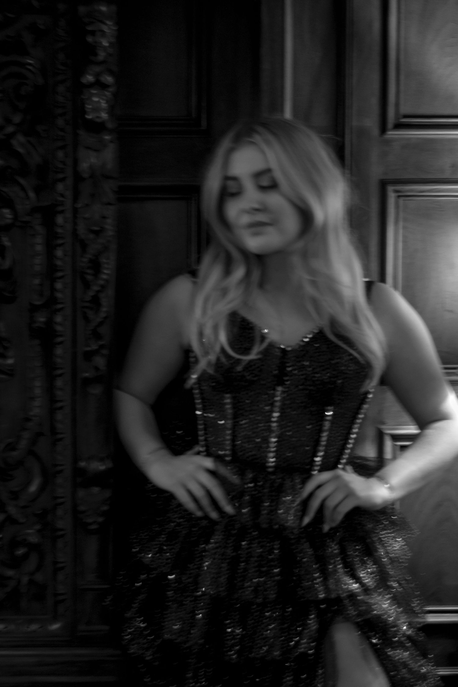 Woman in sequined corset dress posing by ornate wooden door in black and white photo.