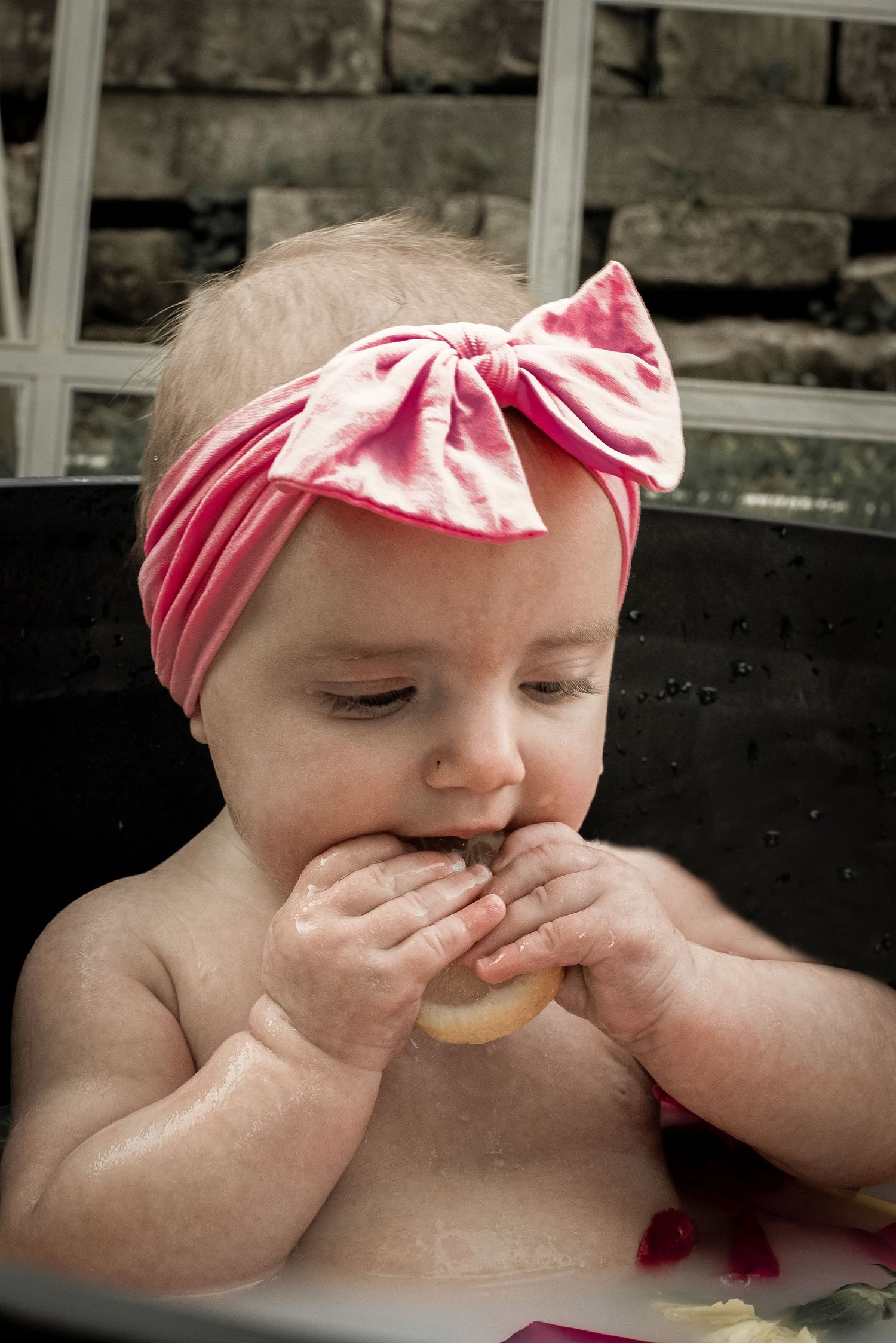 Baby girl with pink bow headband sits in tub eating a donut during cake smash session.