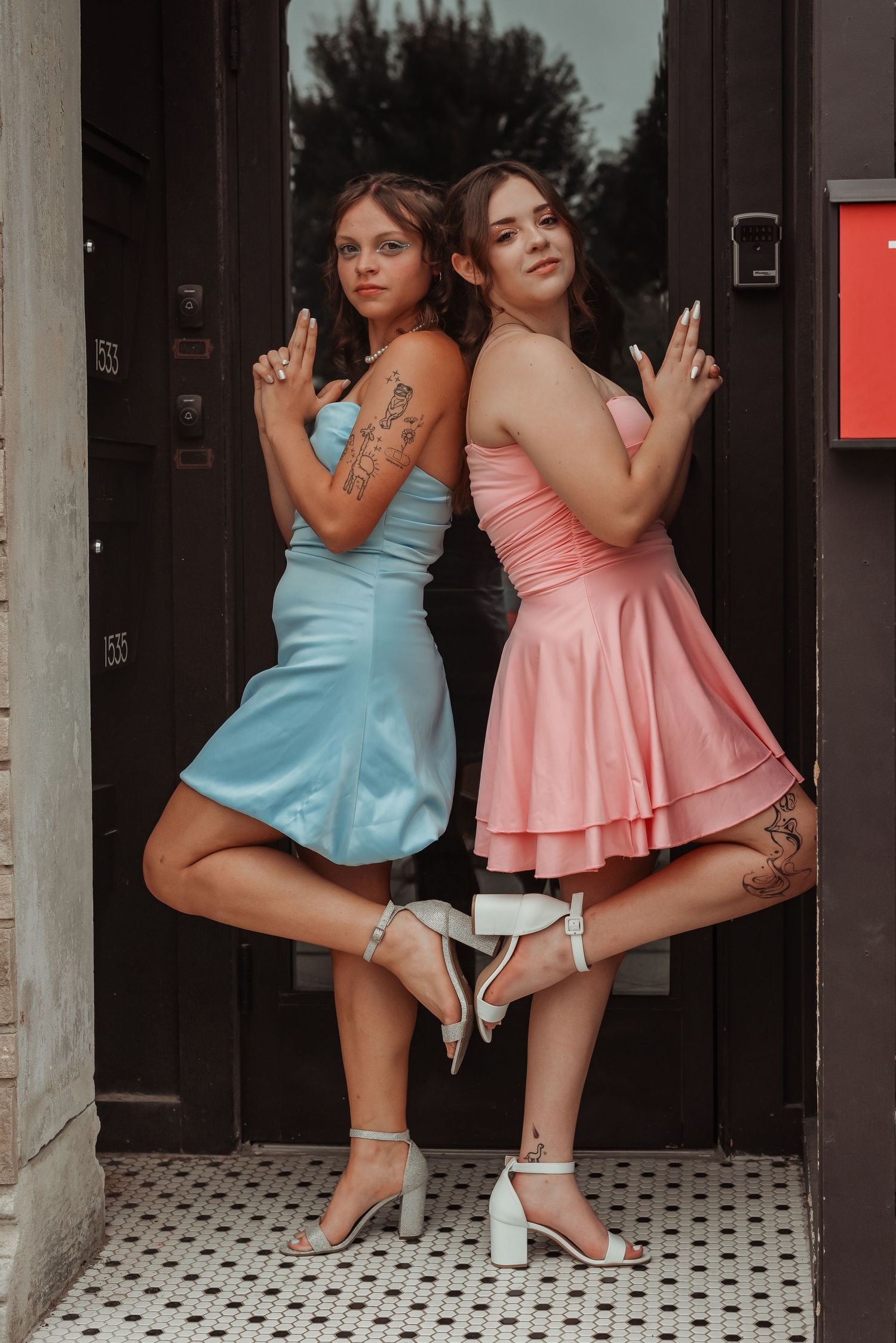 Two women in blue and pink satin dresses posing back-to-back in a doorway.