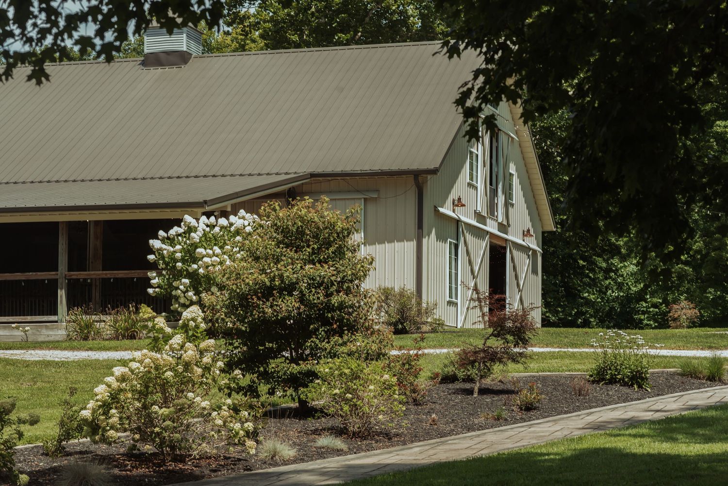 Charming white barn wedding venue surrounded by lush green trees and blooming hydrangea bushes.