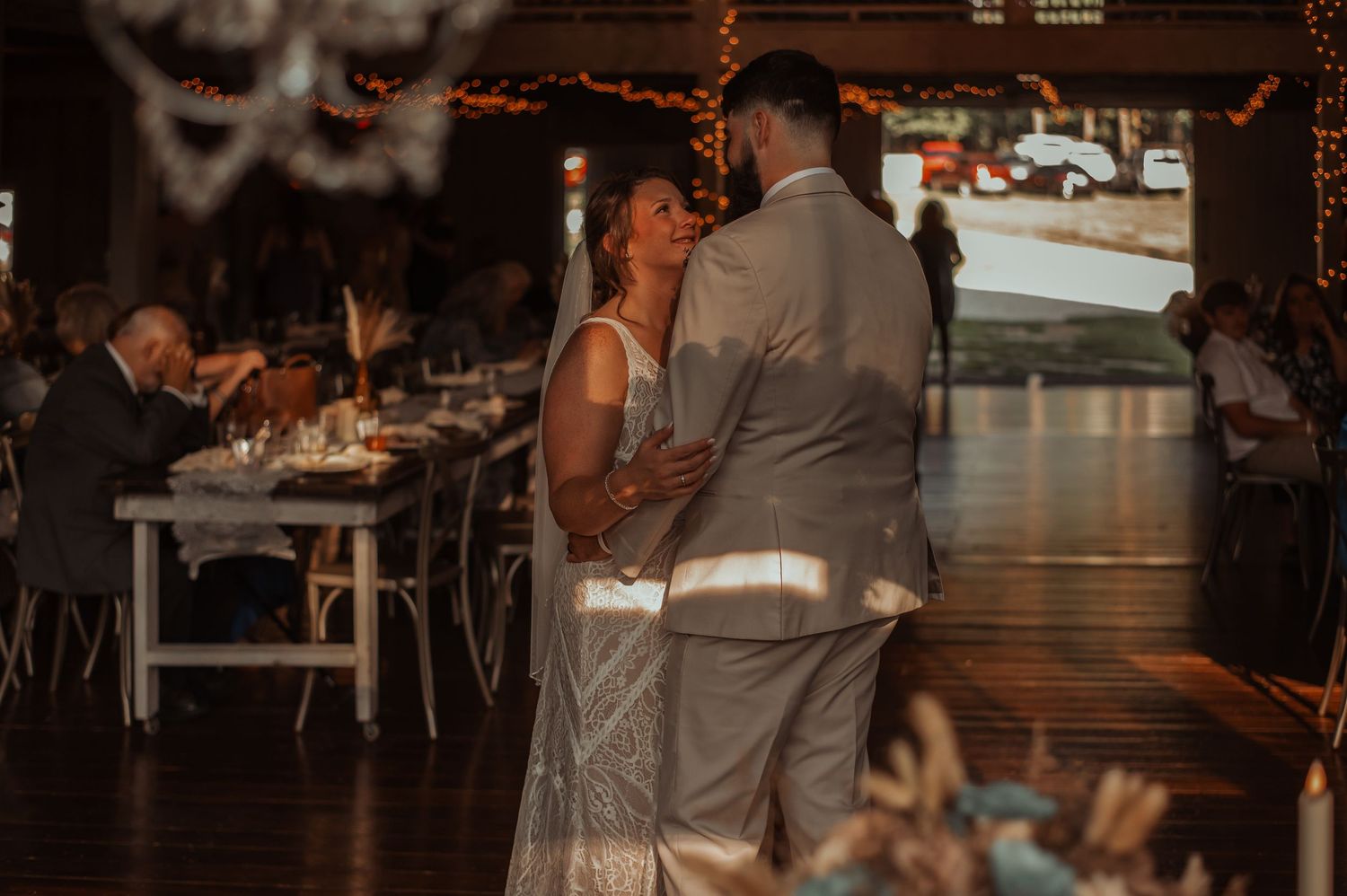 Bride and groom share their first dance in a warmly lit rustic wedding reception venue.