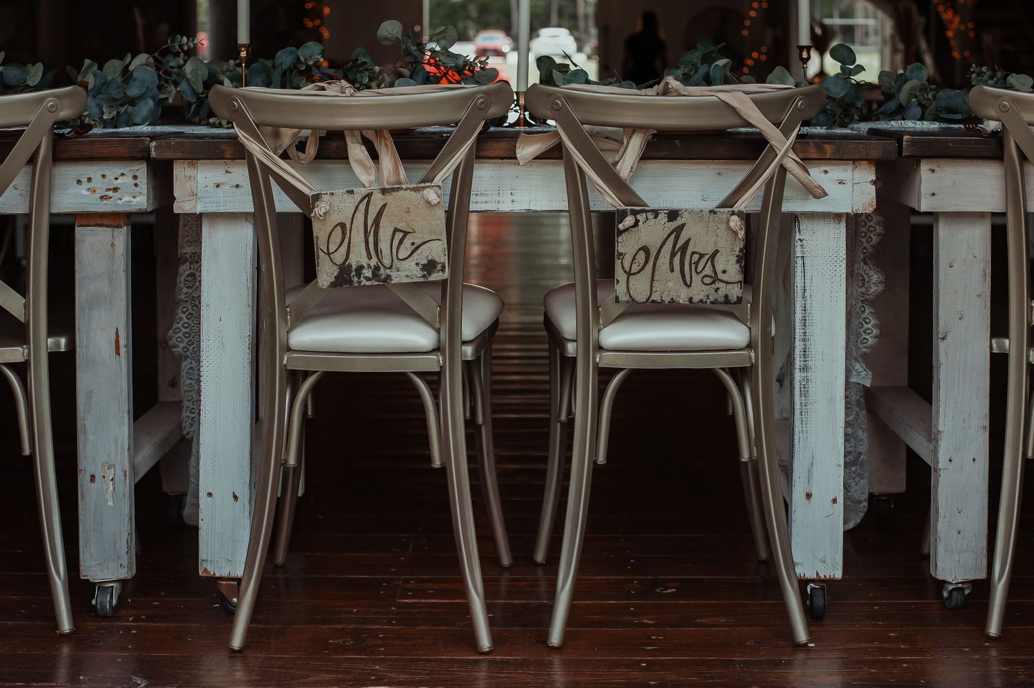 Mr. and Mrs. wooden signs hang on rustic gold cross-back chairs at an elegant wedding reception table.