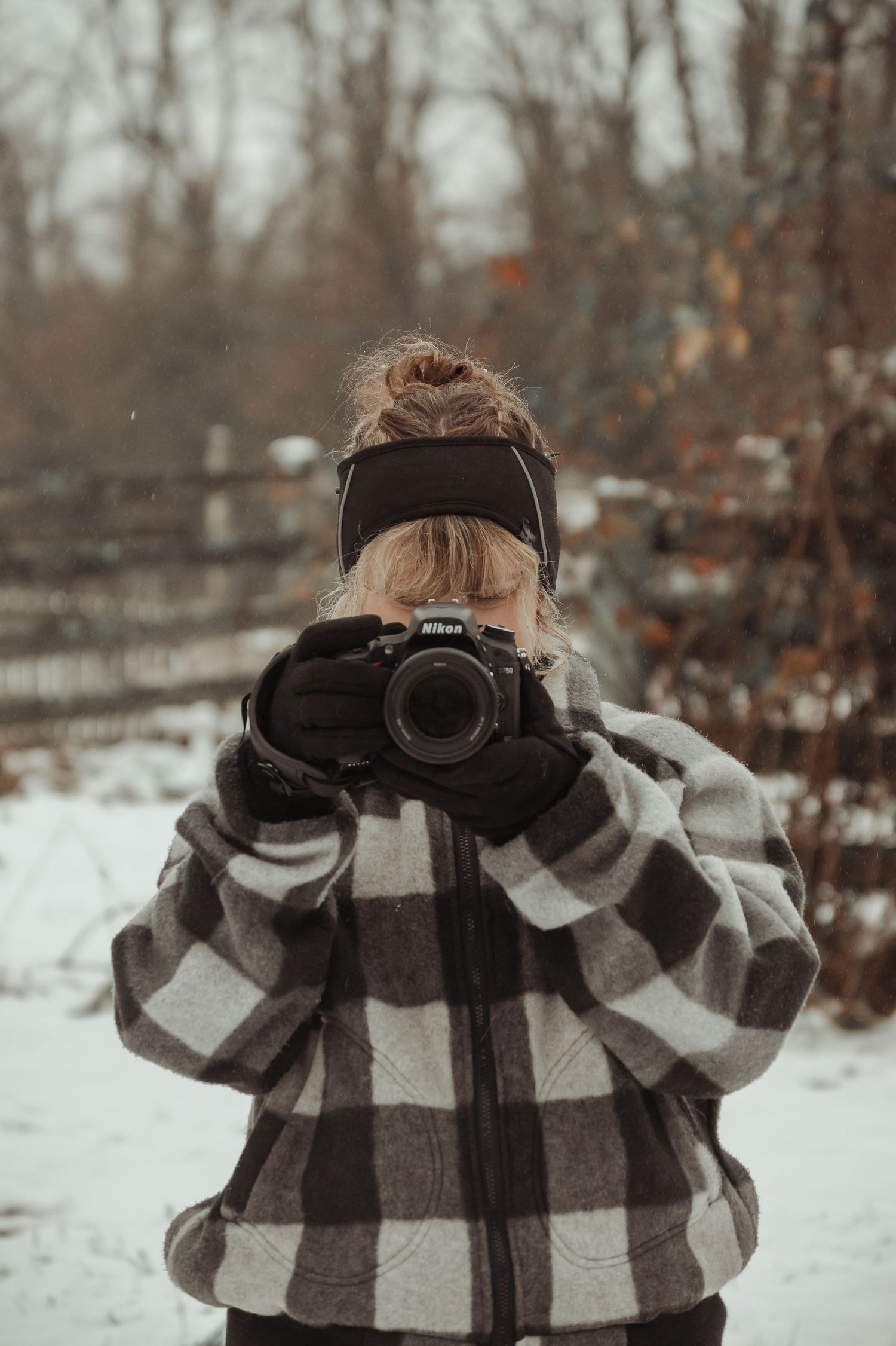 Photographer aiming Nikon camera outdoors in snowy winter landscape.