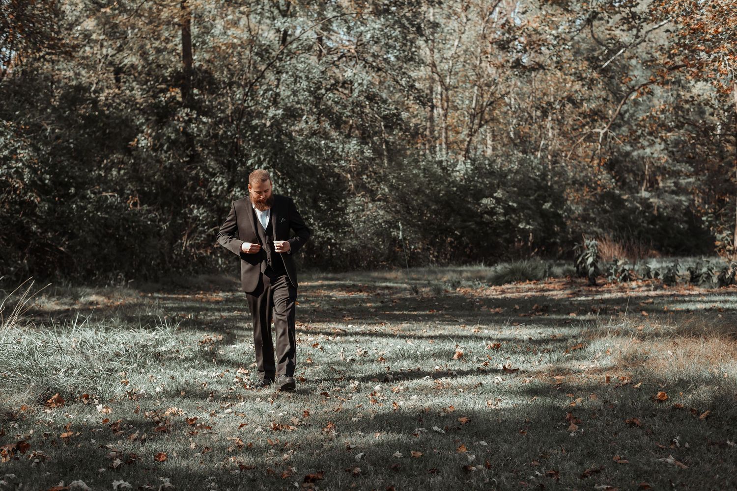 Man in dark suit walking through autumn forest clearing.