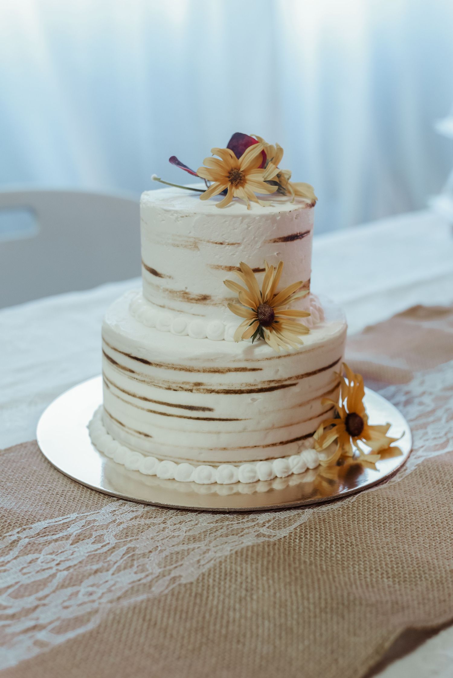 Two-tier white wedding cake decorated with yellow sunflowers on a burlap and lace table runner.