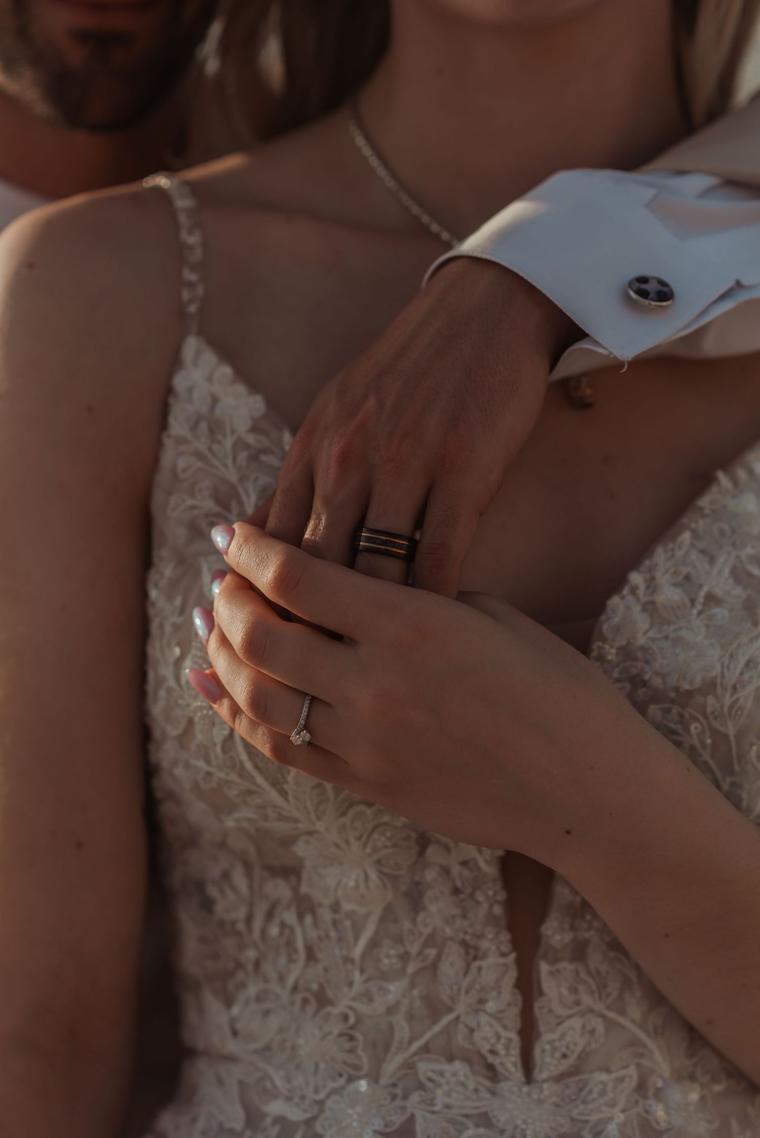 Bride and groom holding hands closeup showing wedding rings, engagement ring, and elegant cufflinks on wedding day.