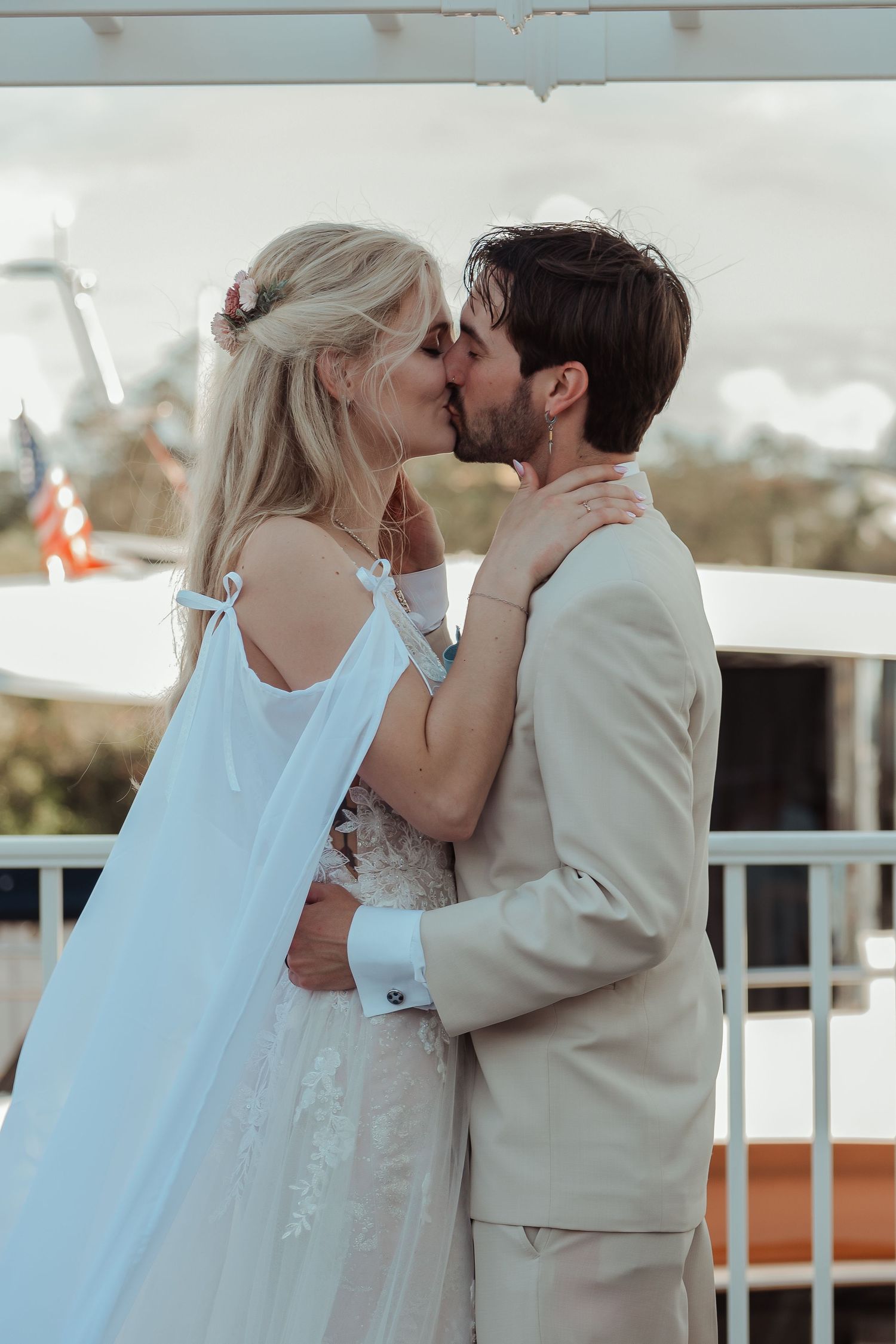 Bride and groom sharing romantic first kiss on waterfront venue balcony on their wedding day.