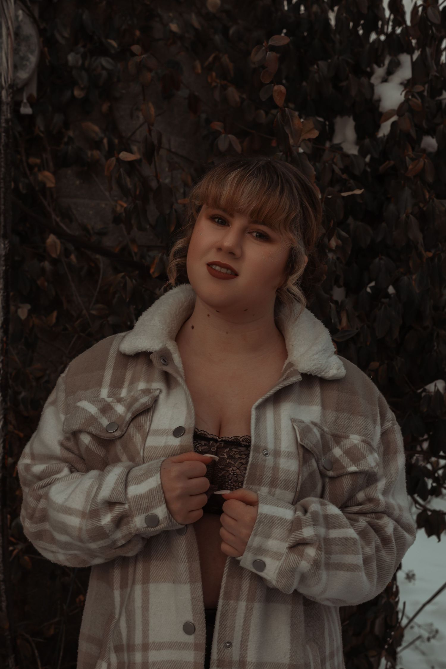 Plus-size woman in plaid shacket and lace bra posing outdoors in winter.