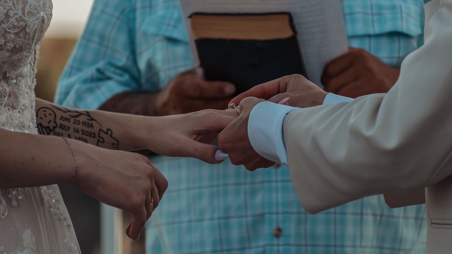 Close-up of bride and groom exchanging wedding rings during ceremony with officiant holding bible.