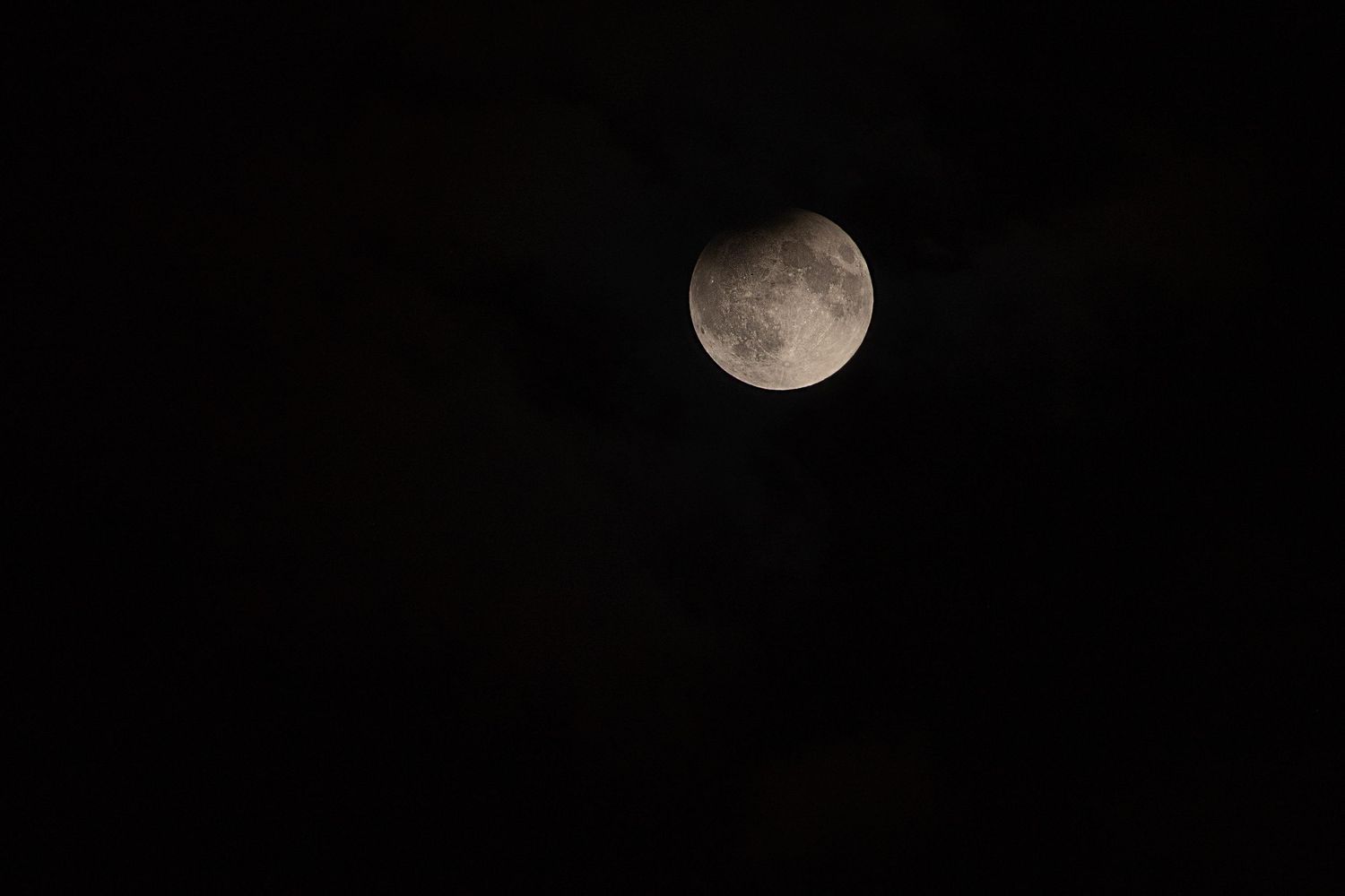 A full moon glowing against a dark night sky with faint clouds visible.