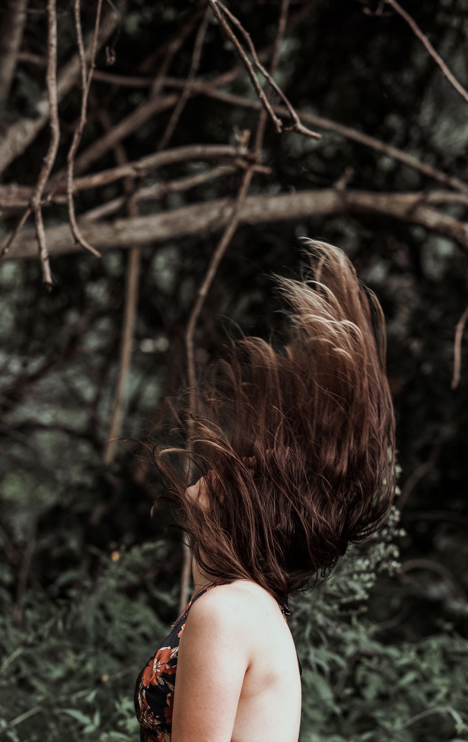 Woman tossing long brown hair in front of woodland background.