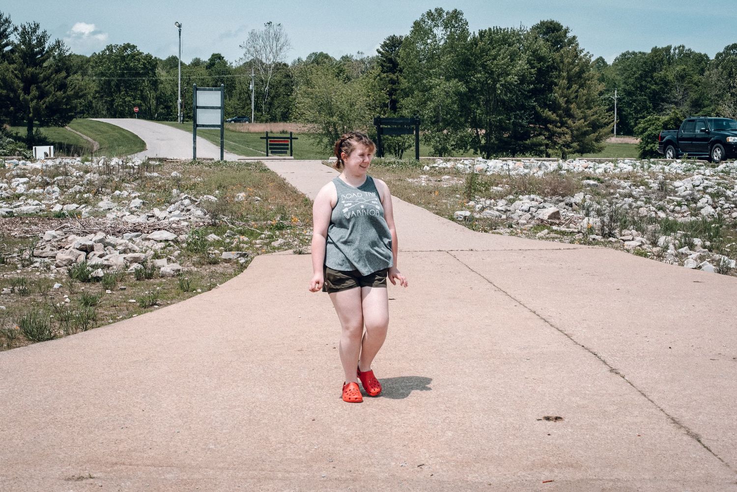 Woman walking alone on paved path in sunny outdoor recreational area.