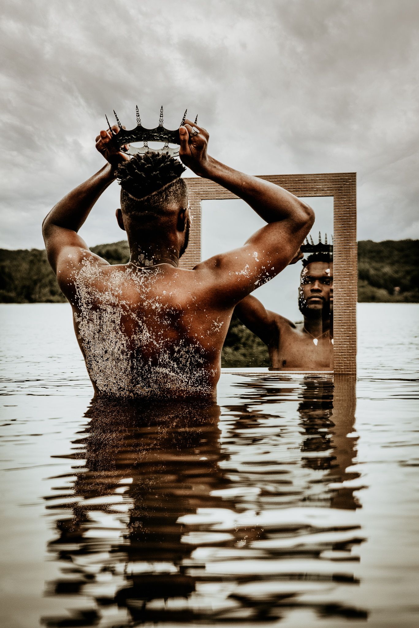 Man placing crown on head while standing in lake with mirror reflection visible.