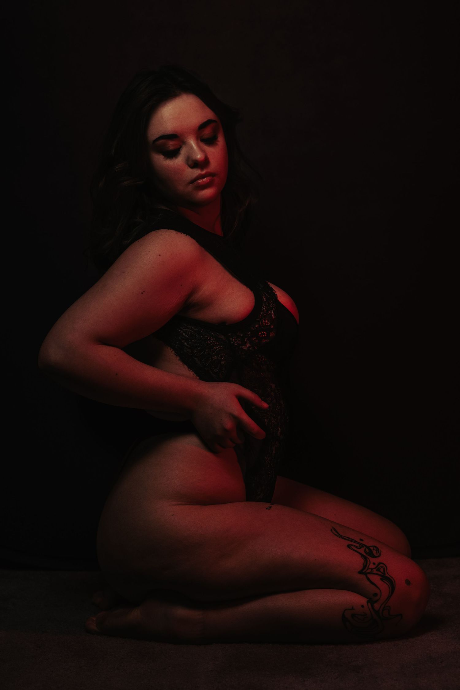 Woman in black lace bodysuit posing in dramatic red studio lighting.