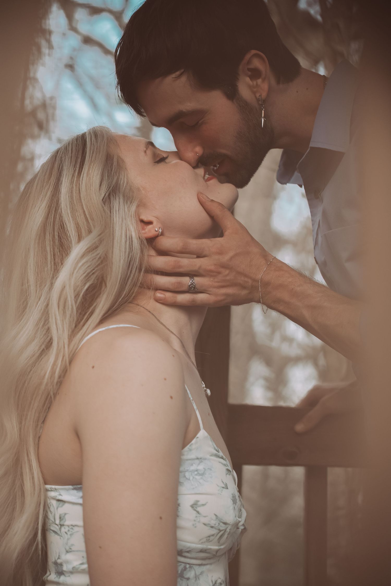 Man gently cupping woman's face for a kiss under a pergola surrounded by trees.