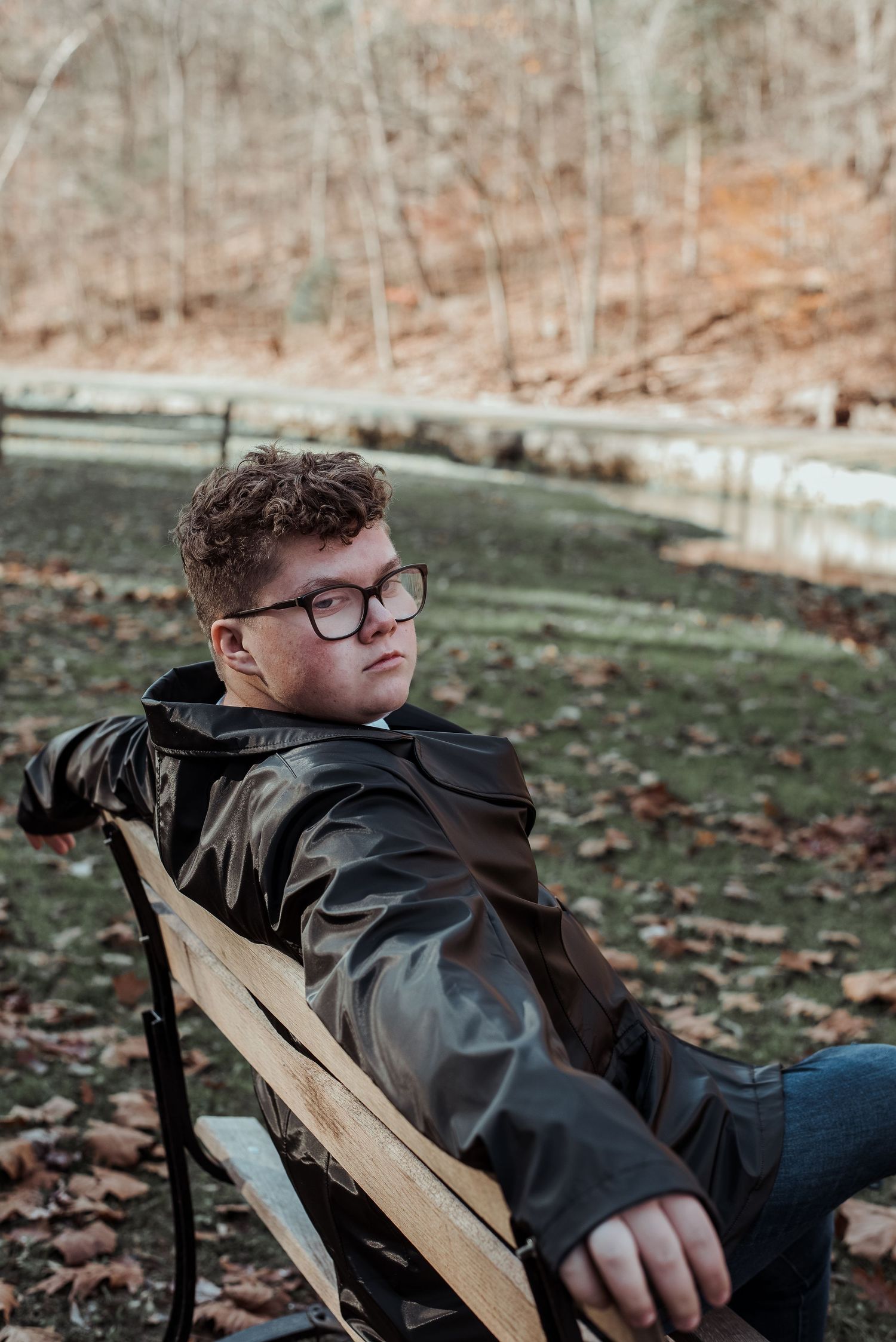 Young man in leather jacket sitting on bench in autumn park.