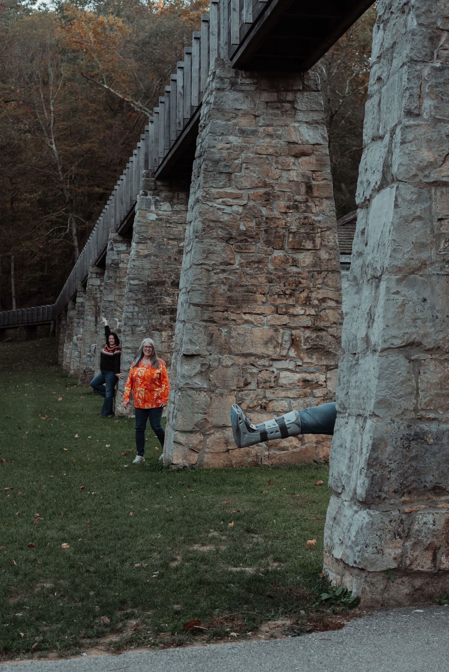 Two women walking near historic stone bridge pillars with a cannon in autumn.