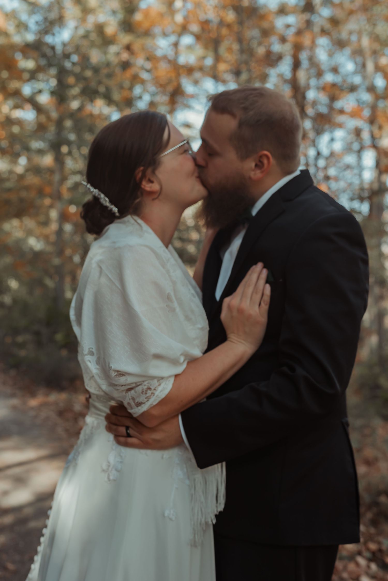 Bride and bearded groom sharing first kiss in autumn woodland.