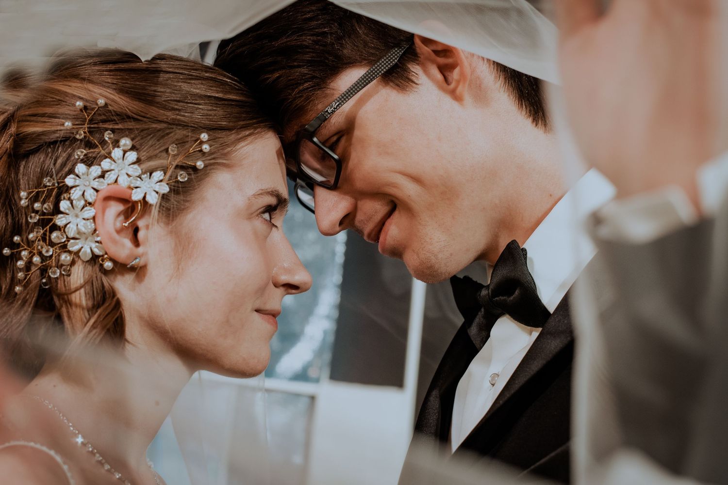 Intimate moment of bride and groom touching foreheads tenderly beneath a wedding veil.