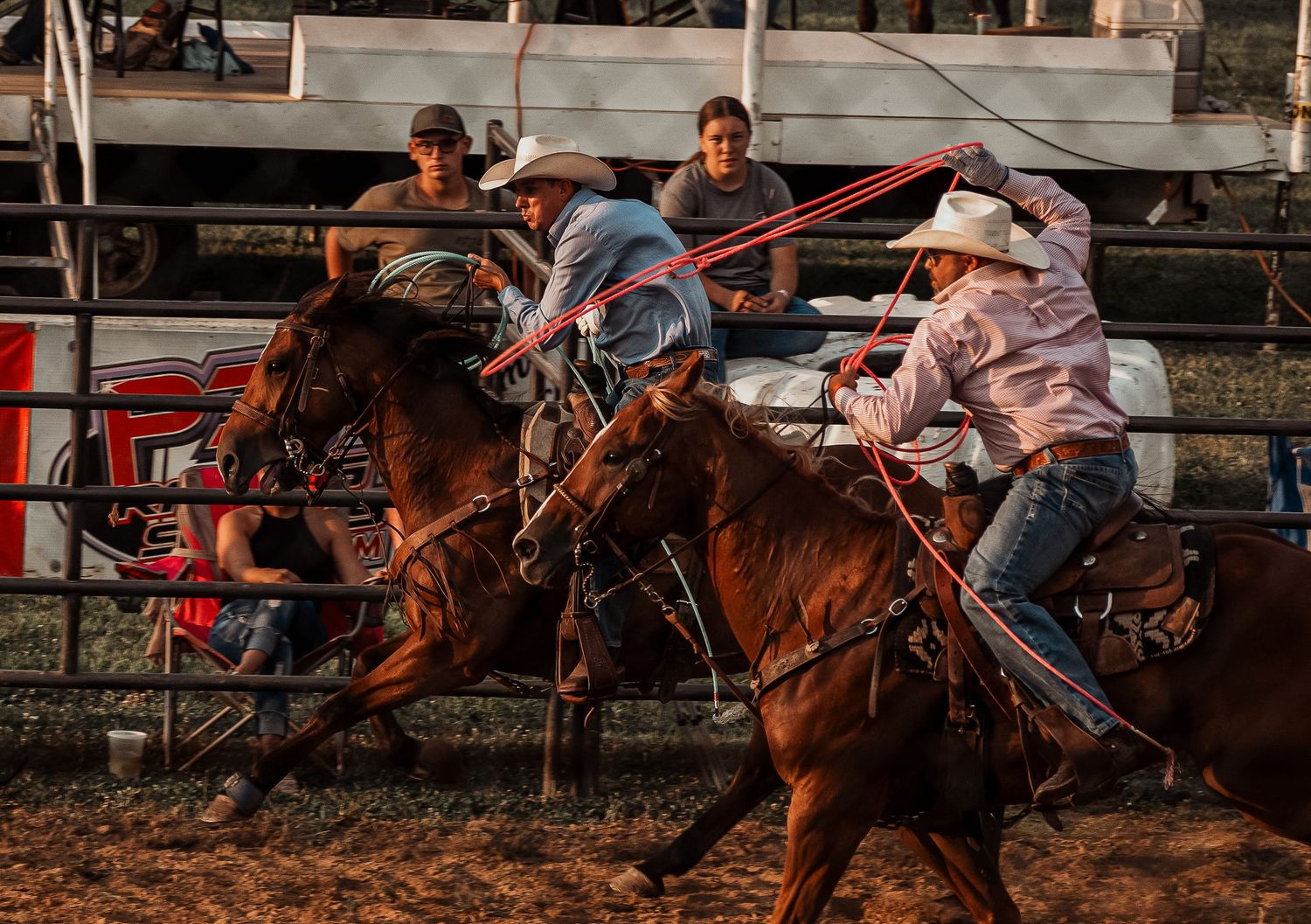 Cowboys on horseback compete in team roping event at a traditional outdoor rodeo arena.