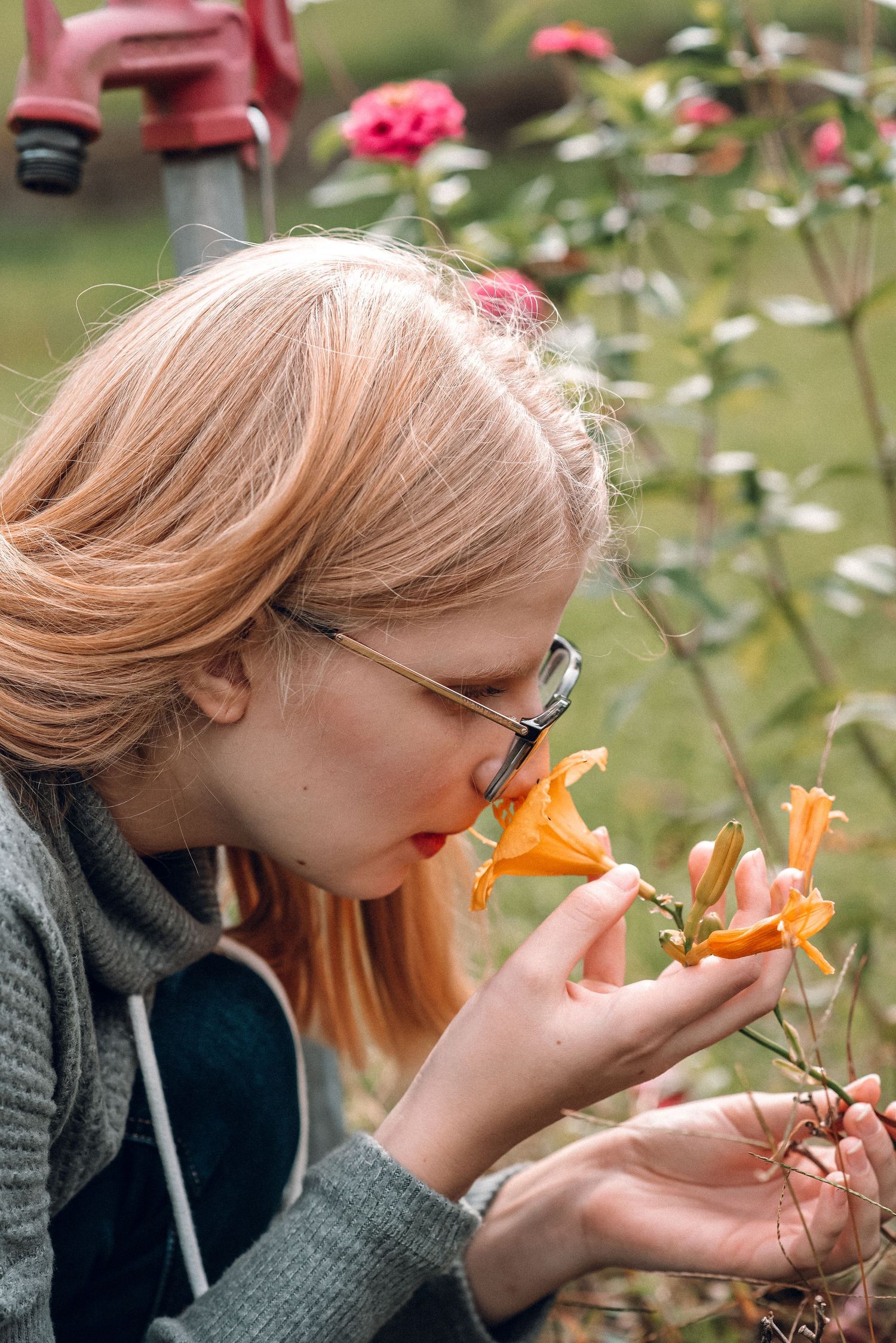Young woman with glasses and red lips smelling orange lily flower in garden setting.