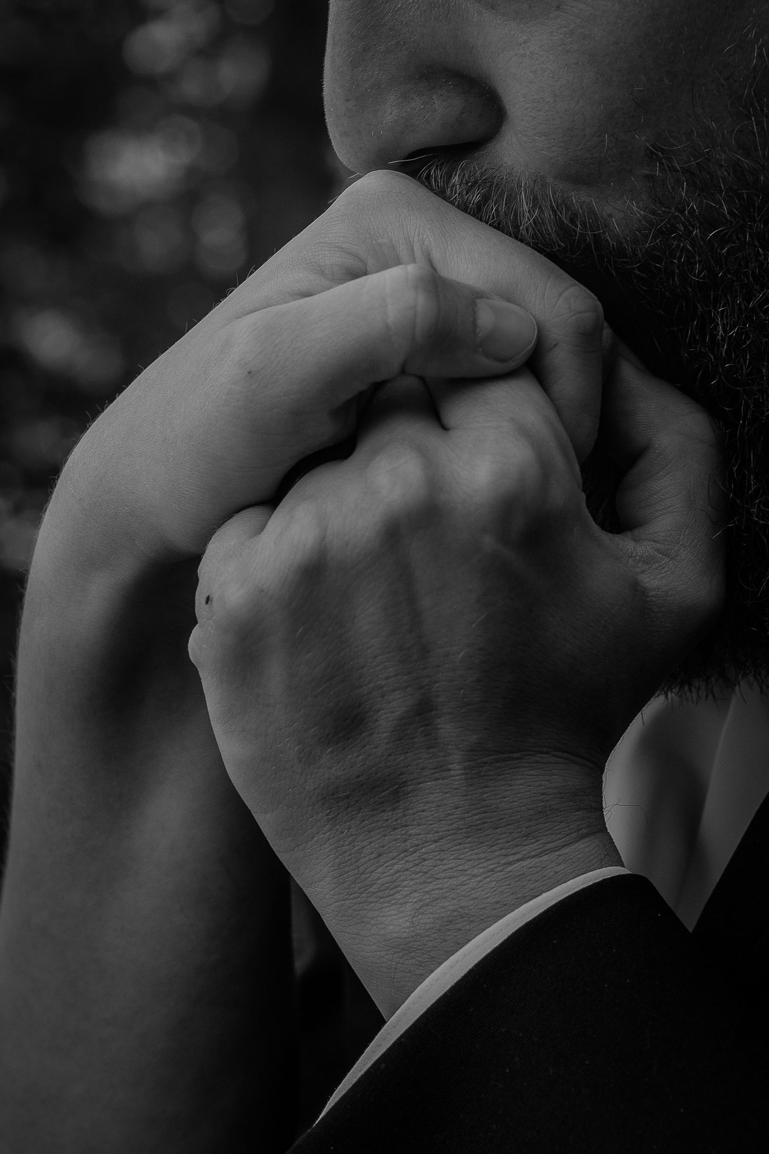 Black and white close-up of groom kissing bride's clasped hands.