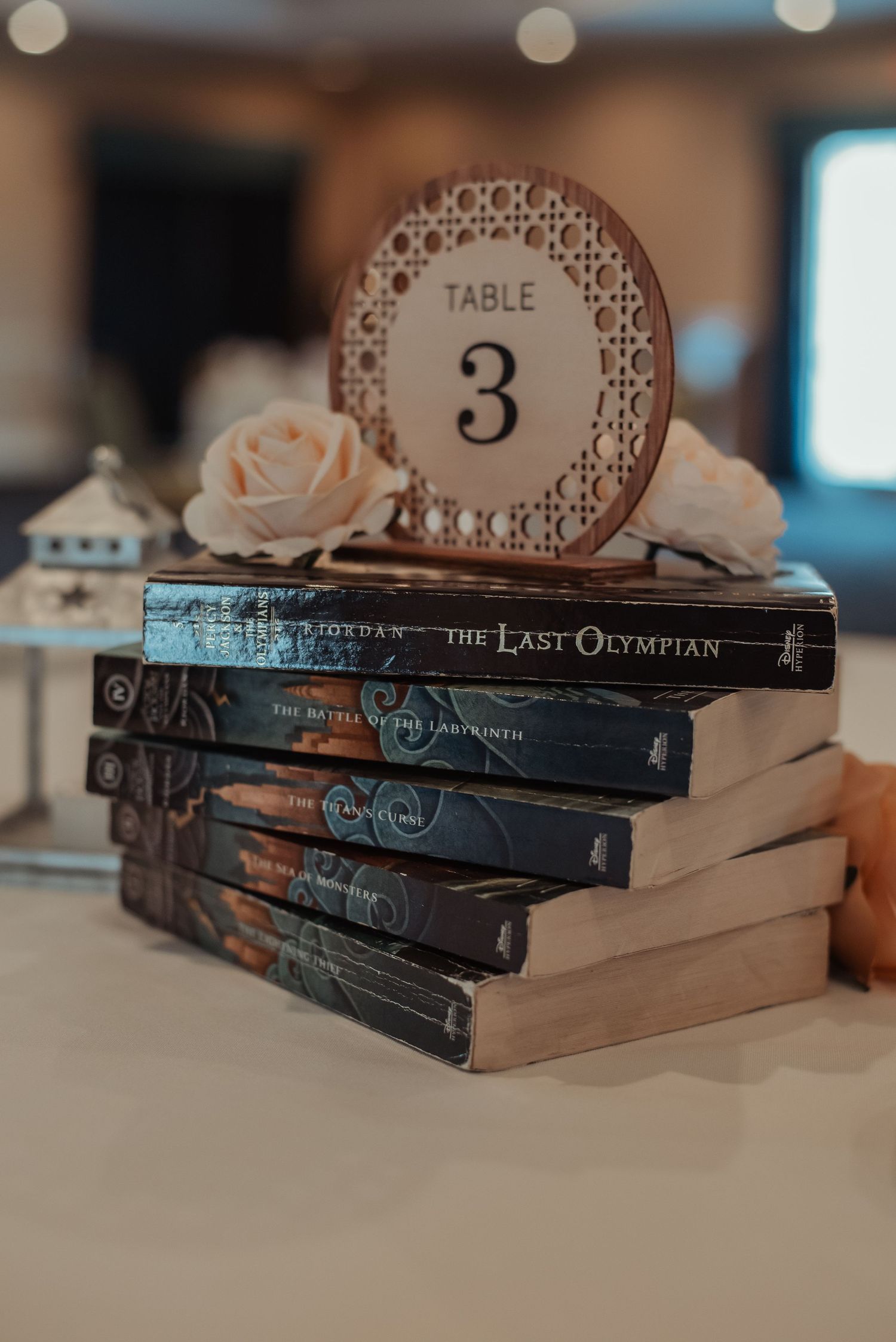 Creative wedding table number display using stacked Percy Jackson books with a blush rose accent.