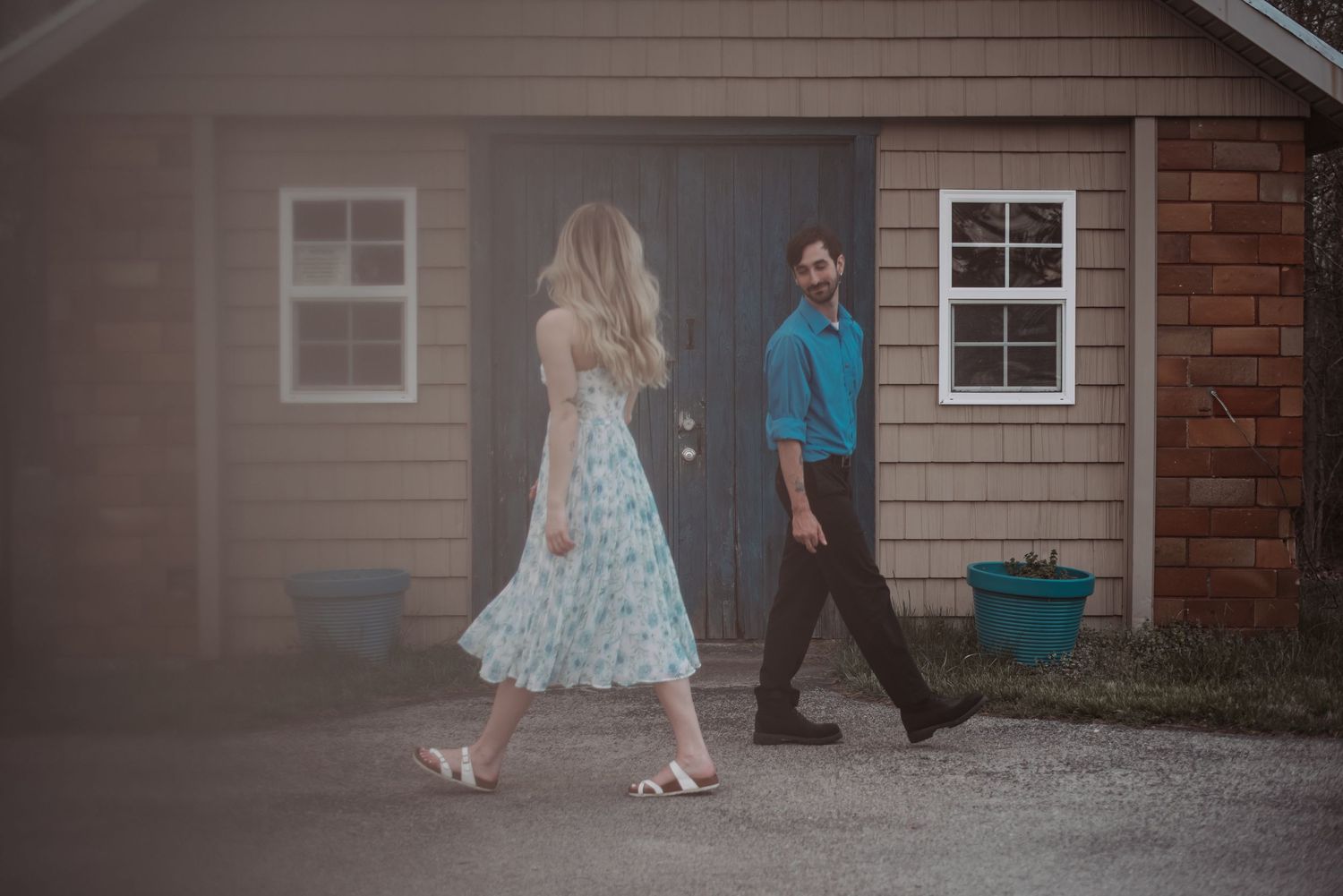 Couple walking toward each other near a rustic wooden building in soft natural light.
