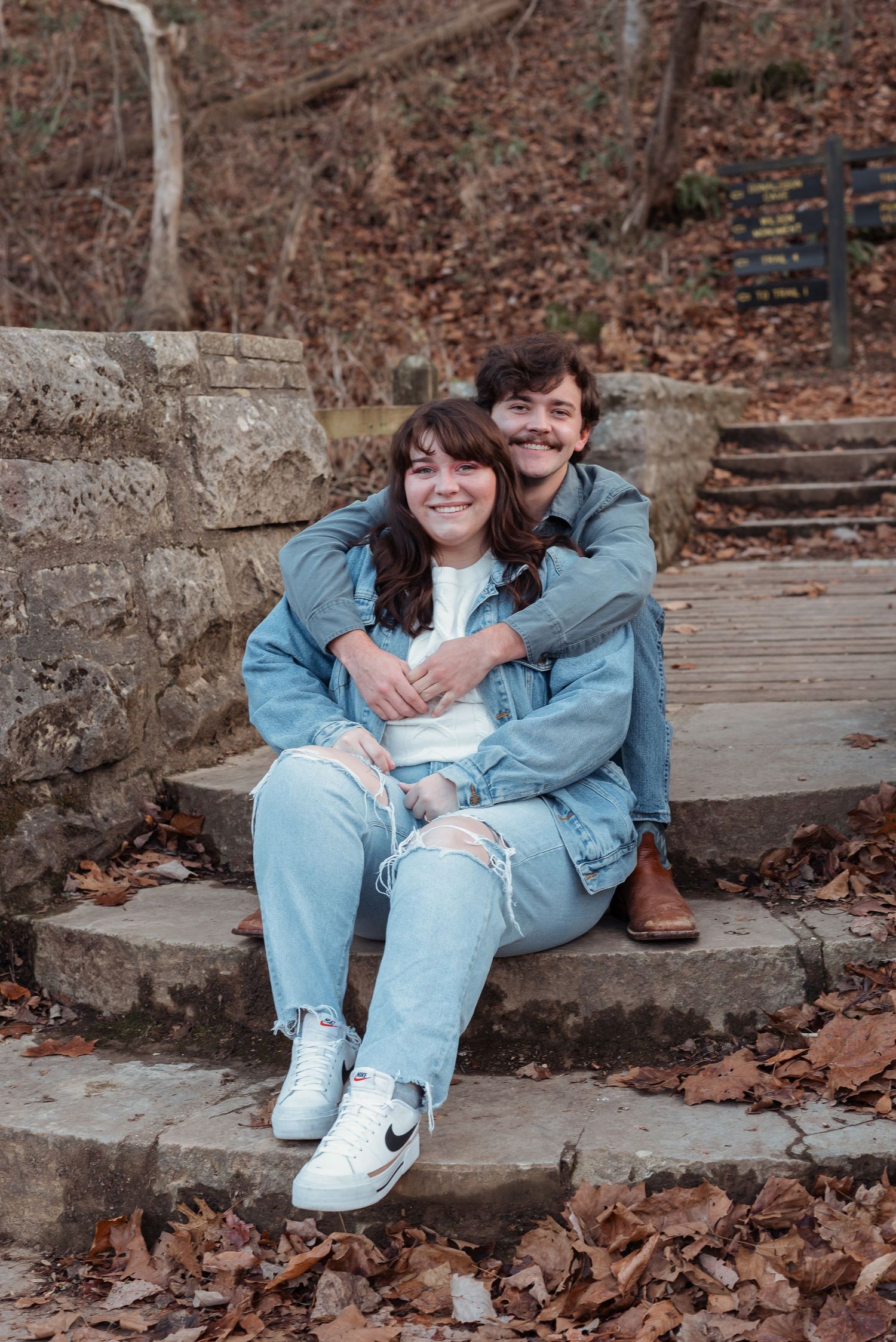 A happy couple sits together on rustic stone steps covered in fallen autumn leaves.