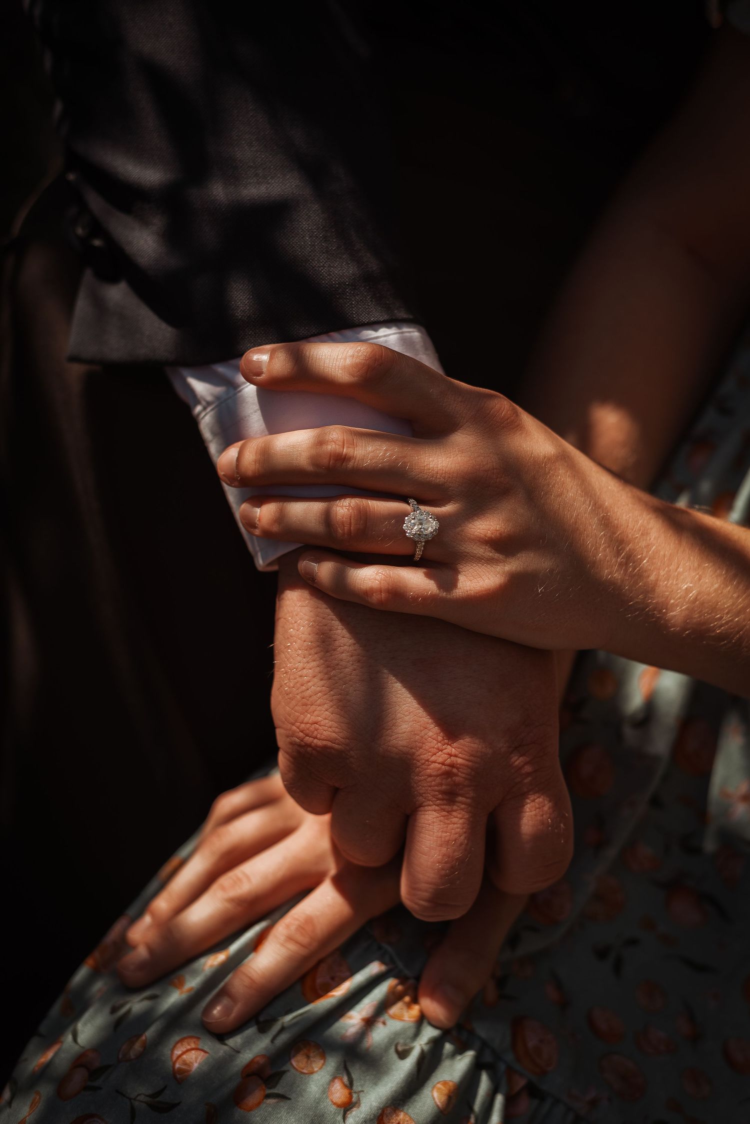 Close-up of a woman's hand resting on a man's wrist, featuring a sparkling diamond engagement ring.