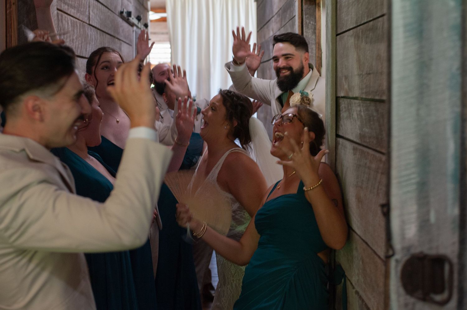 Excited wedding party celebrates with the bride and groom in a joyful indoor gathering moment.