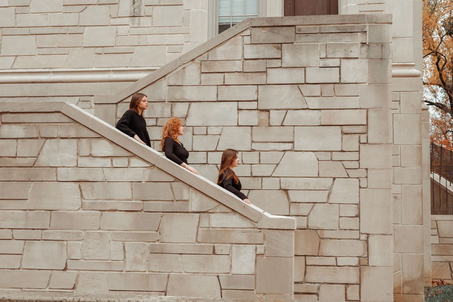 Three women in black outfits walk up outdoor stone staircase beside limestone building.