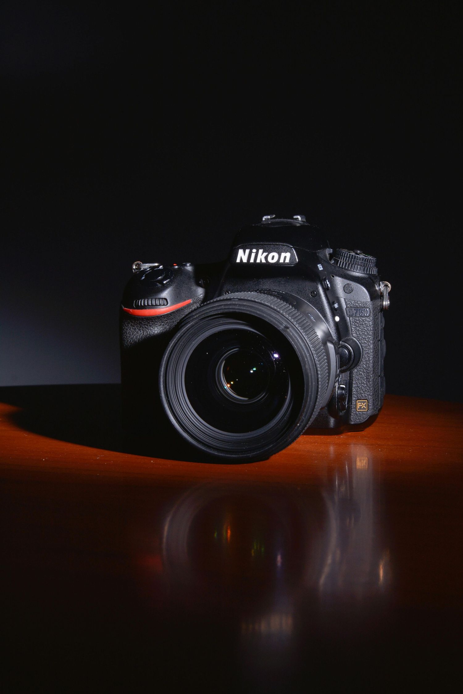 Nikon DSLR camera with lens on wooden surface against dark background with dramatic lighting.
