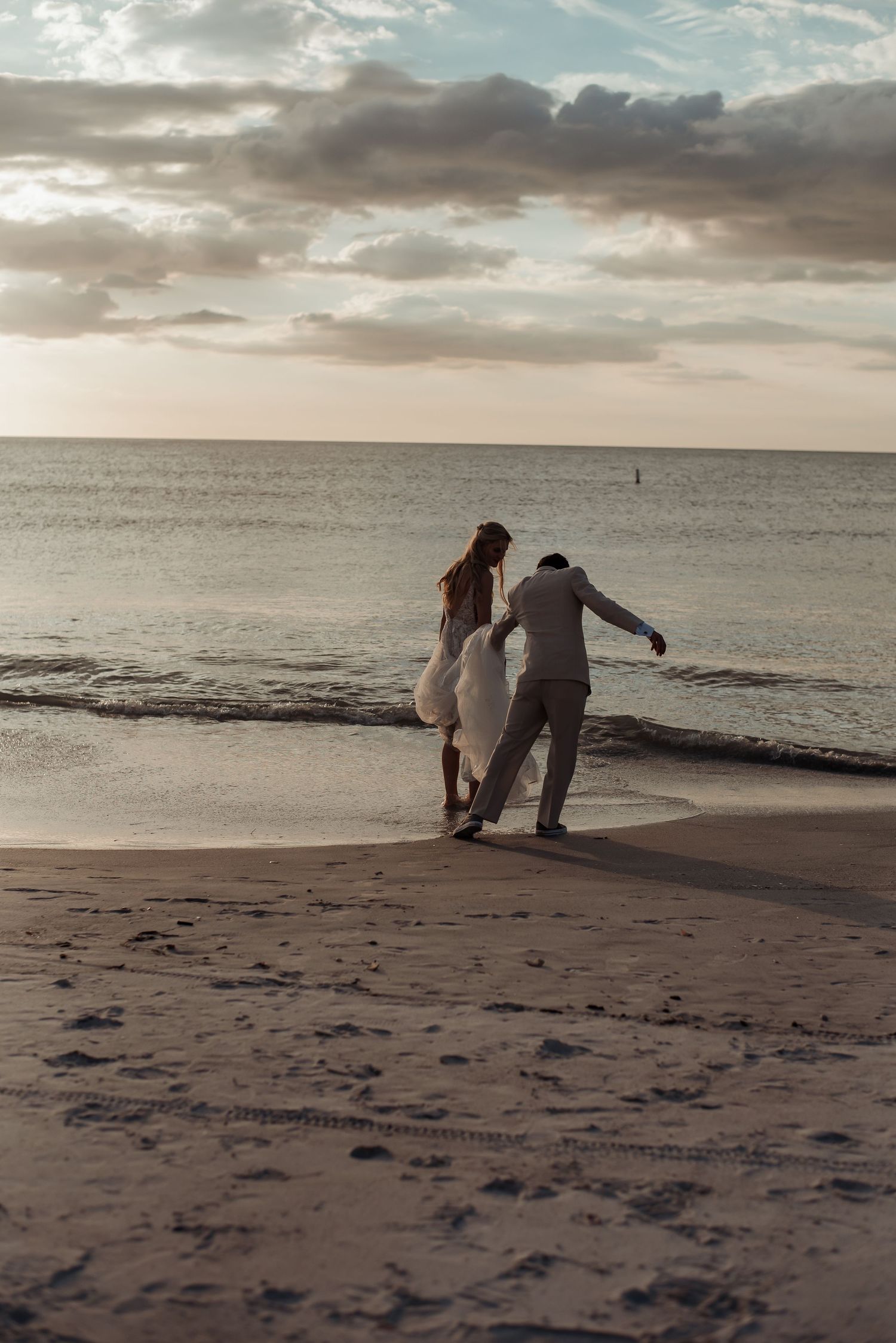 Newlywed couple walking together along ocean shoreline at sunset on their wedding day.