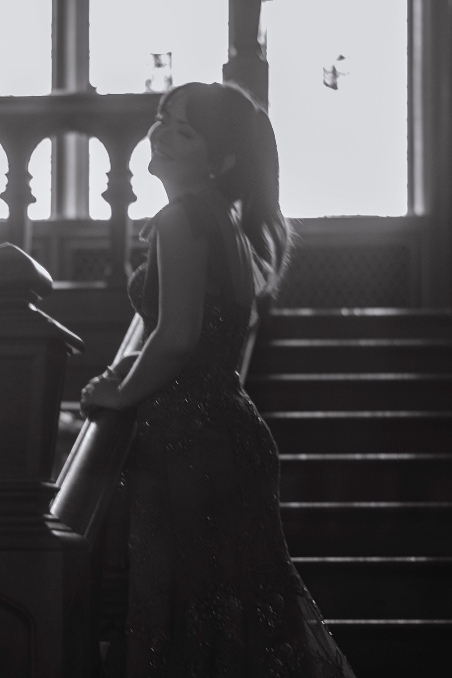 Black and white photo of elegant woman in strapless gown on grand staircase with dramatic backlight.