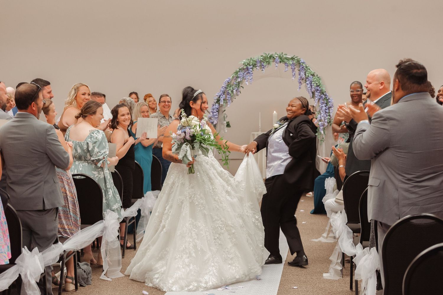 Newlywed couple celebrates joyfully walking down the aisle at their elegant indoor wedding ceremony.