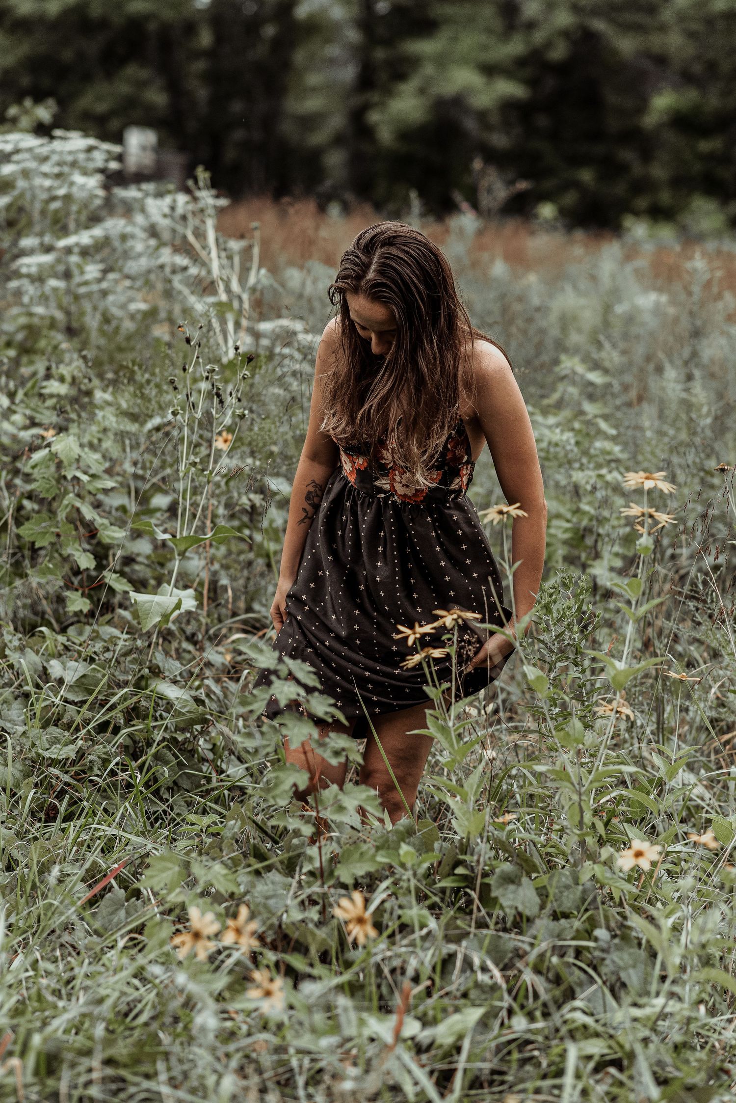 Young woman in black floral dress walking through wildflower meadow.