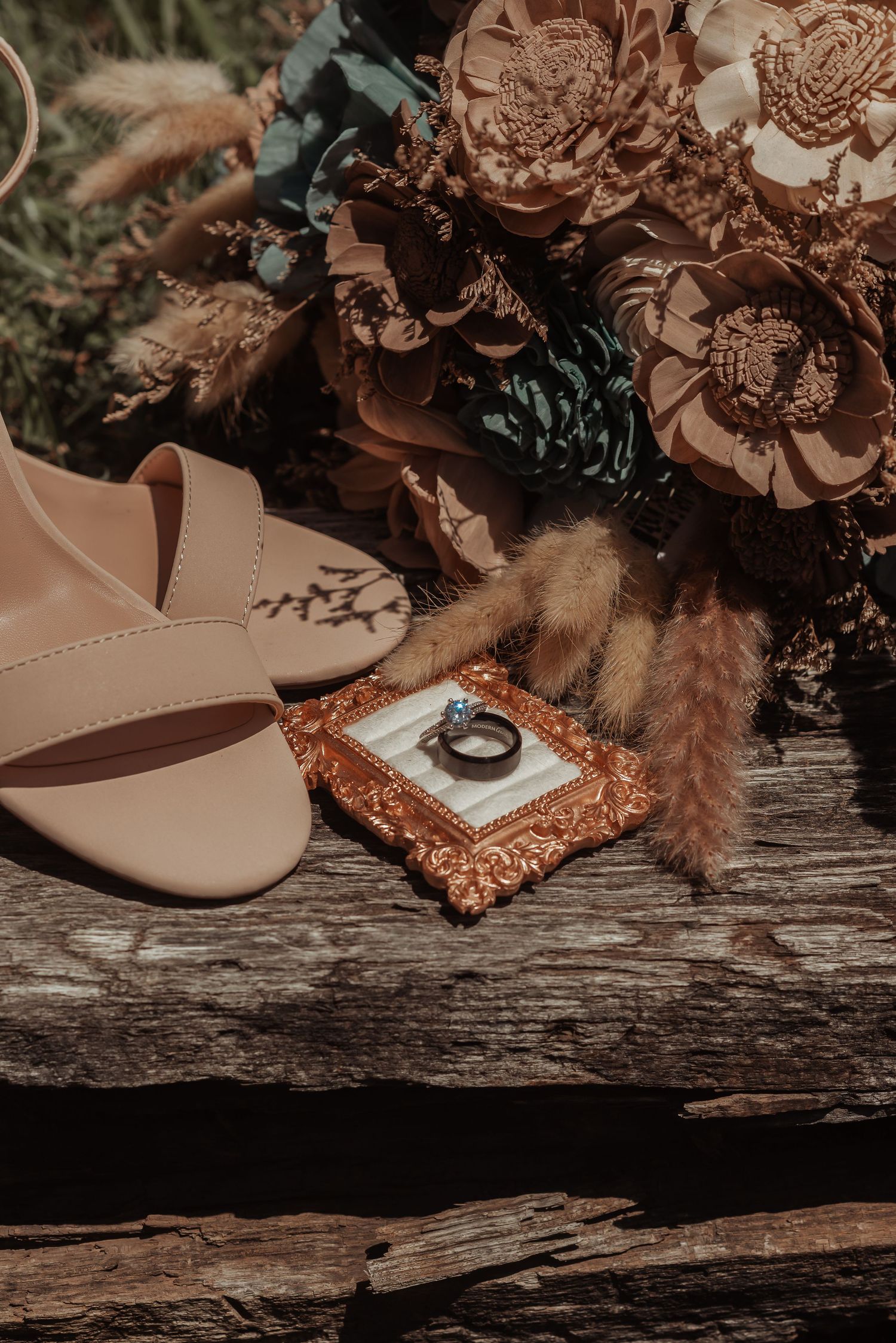 Wedding flat lay featuring nude heels, a ring in ornate box, and a rustic floral bouquet.