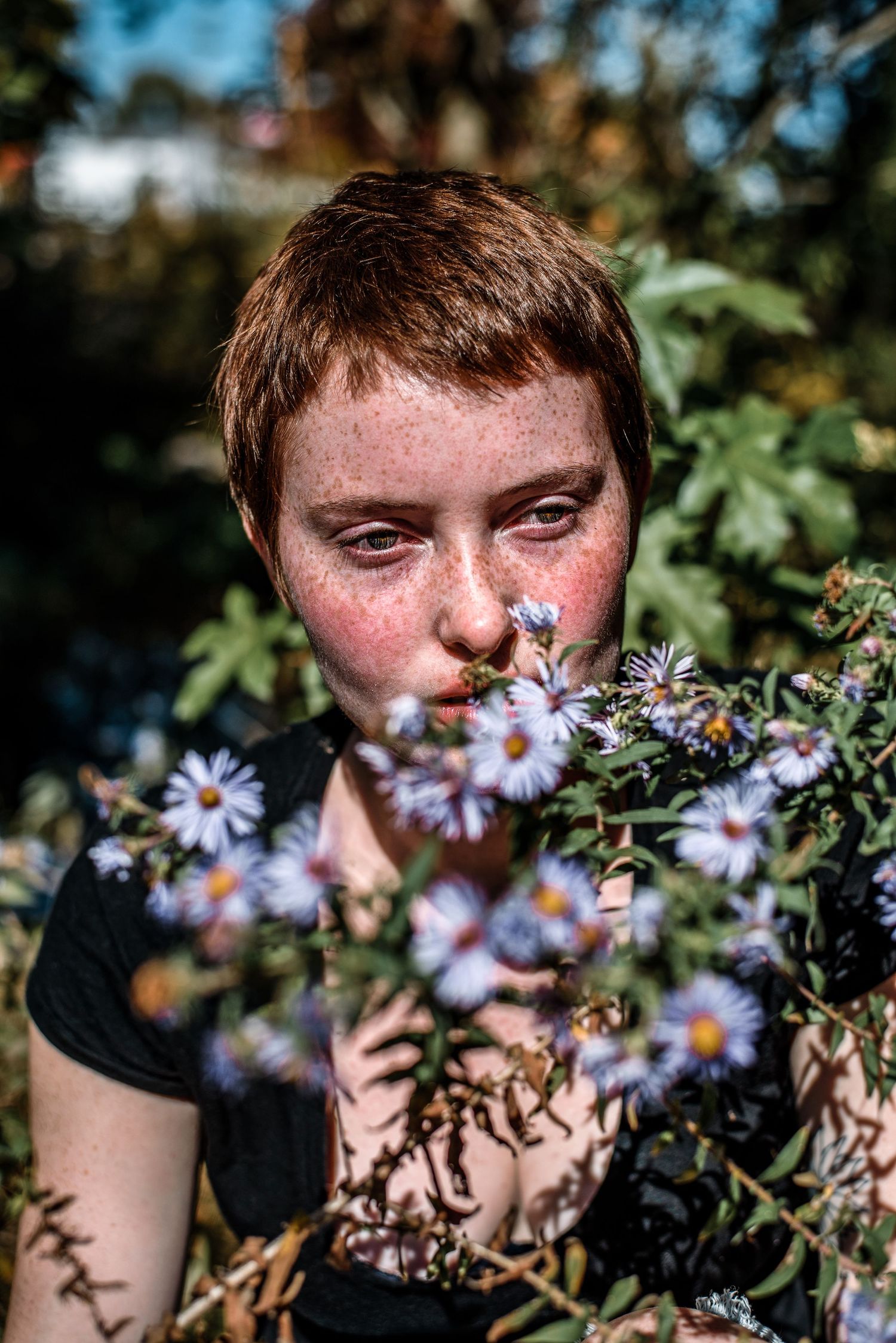 Freckled redhead with short hair smelling wildflowers in a garden.