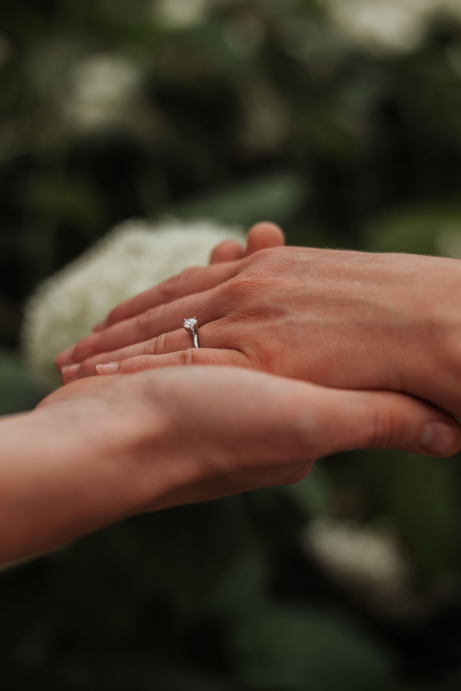 Close-up of two hands held together, showcasing a delicate solitaire diamond engagement ring.