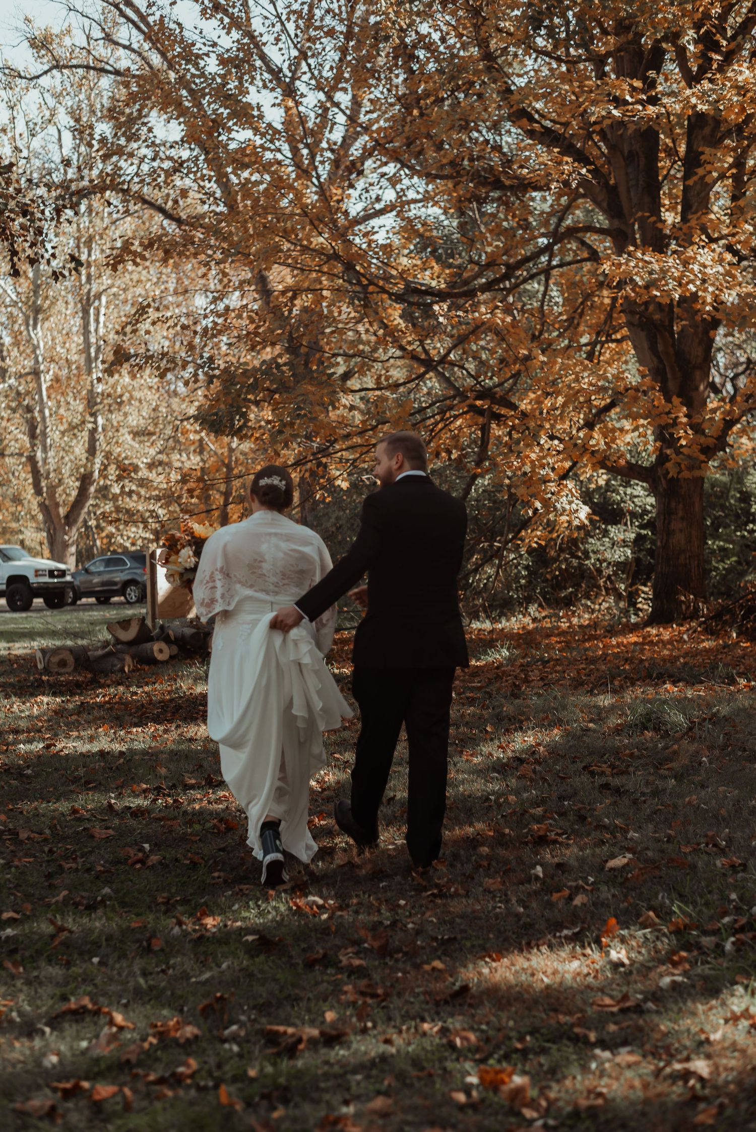 Newlyweds walking hand in hand under golden autumn trees.