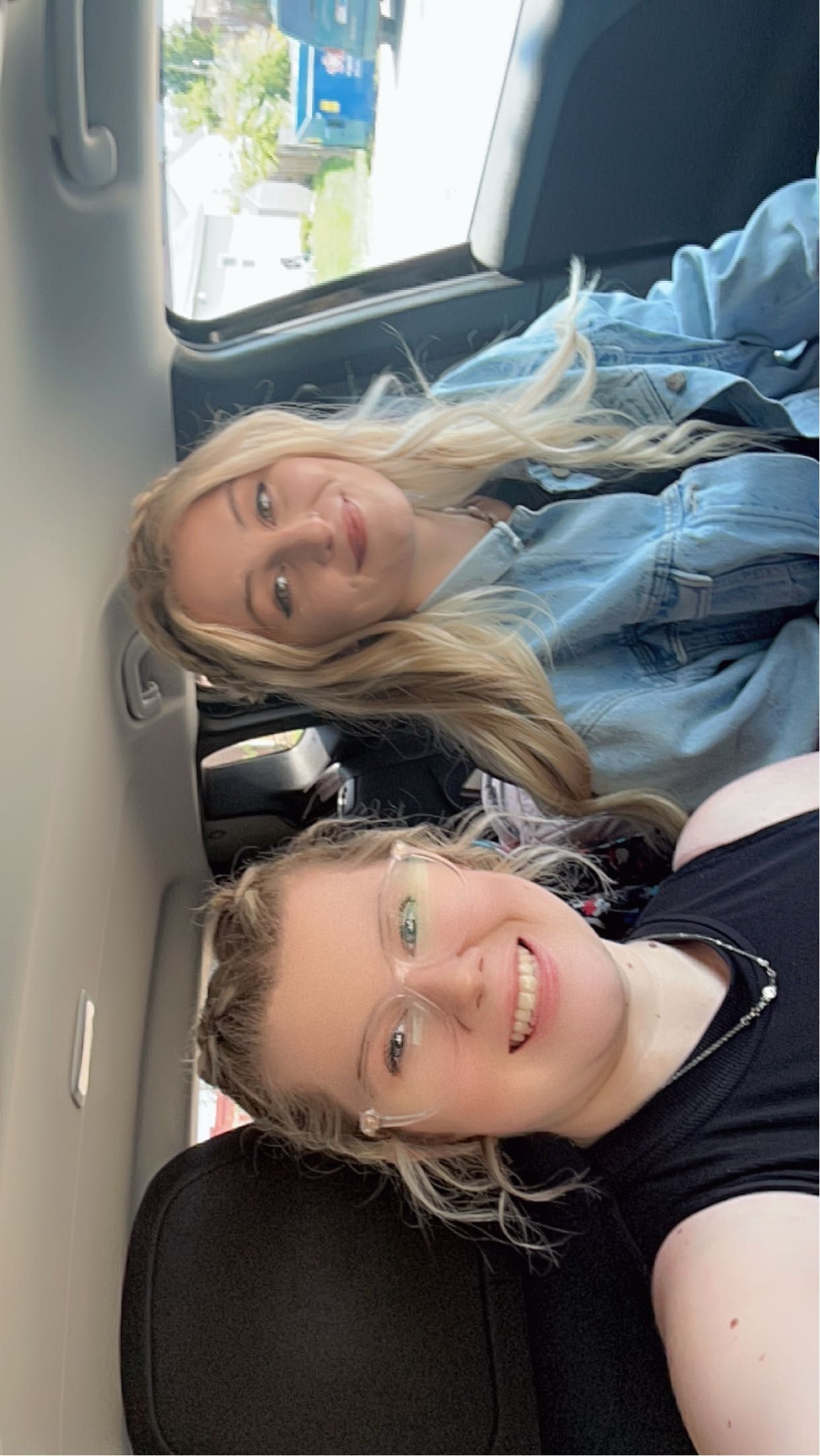 Two young blonde women taking a selfie together inside a car.