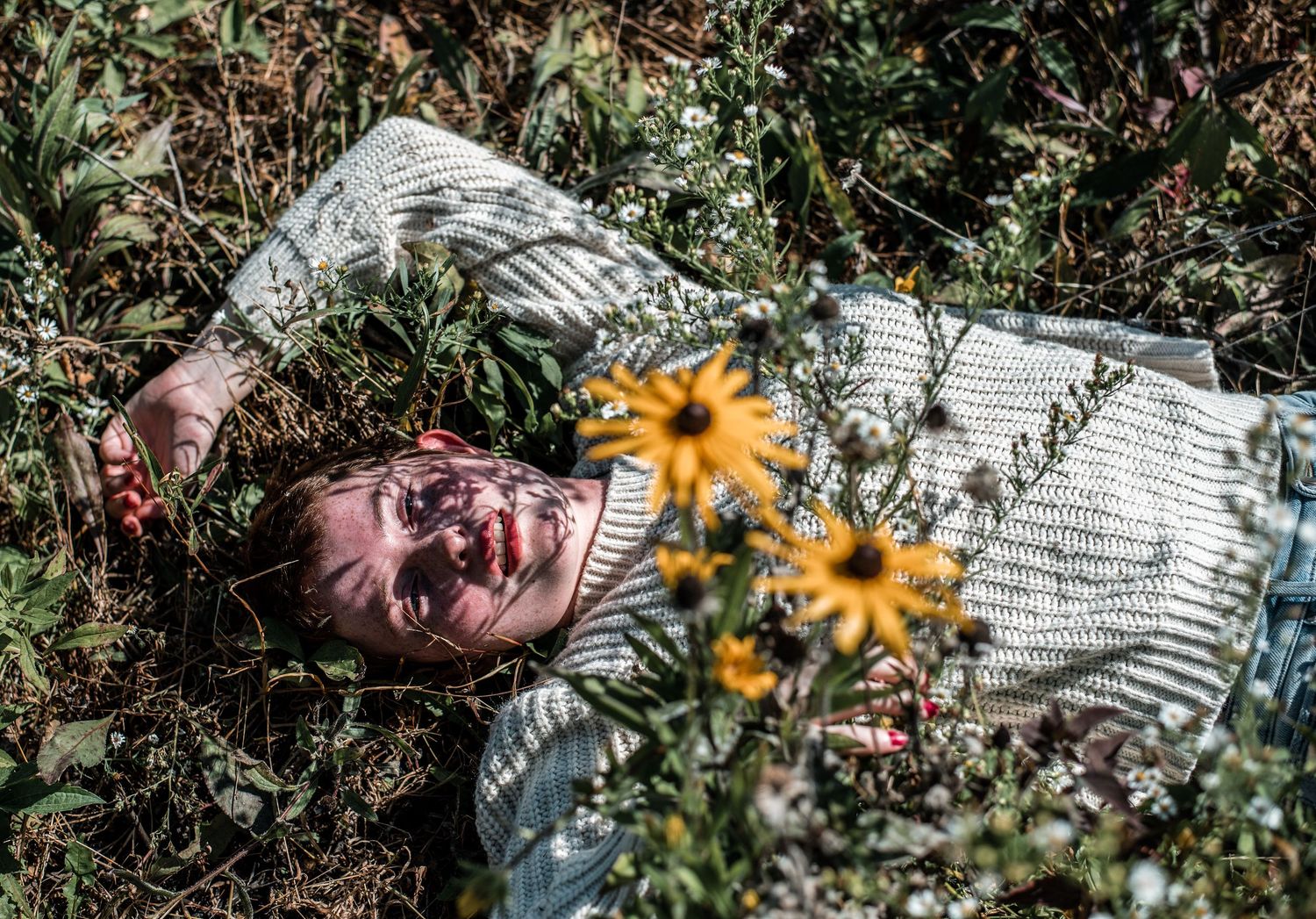 Person in white sweater lying in a field of grass and yellow flowers.