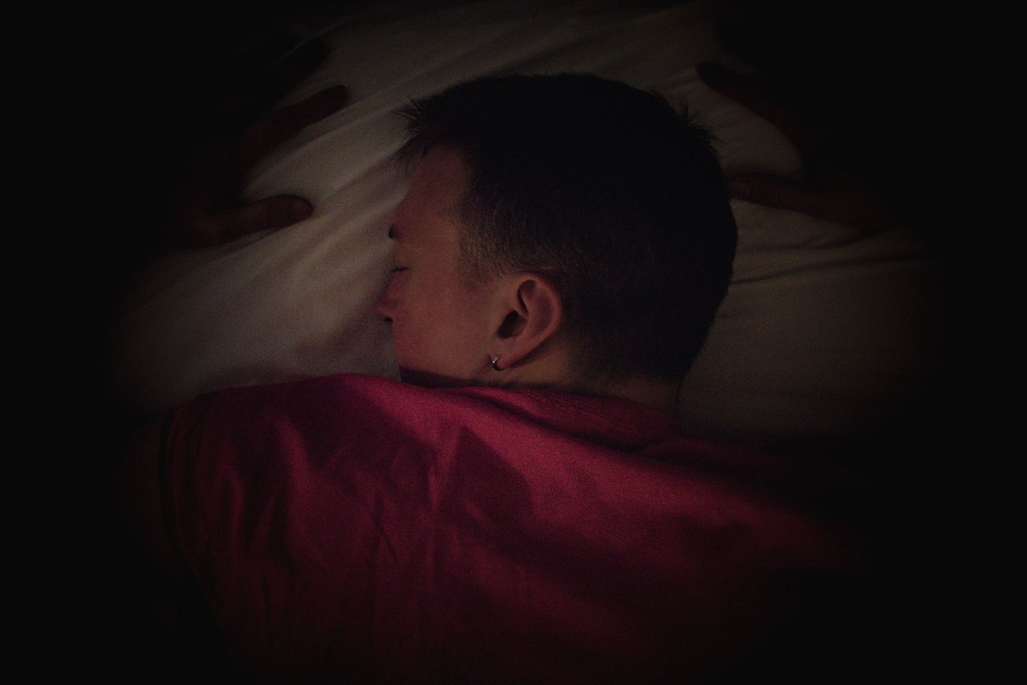 Dimly lit photo of someone resting on red bedding.