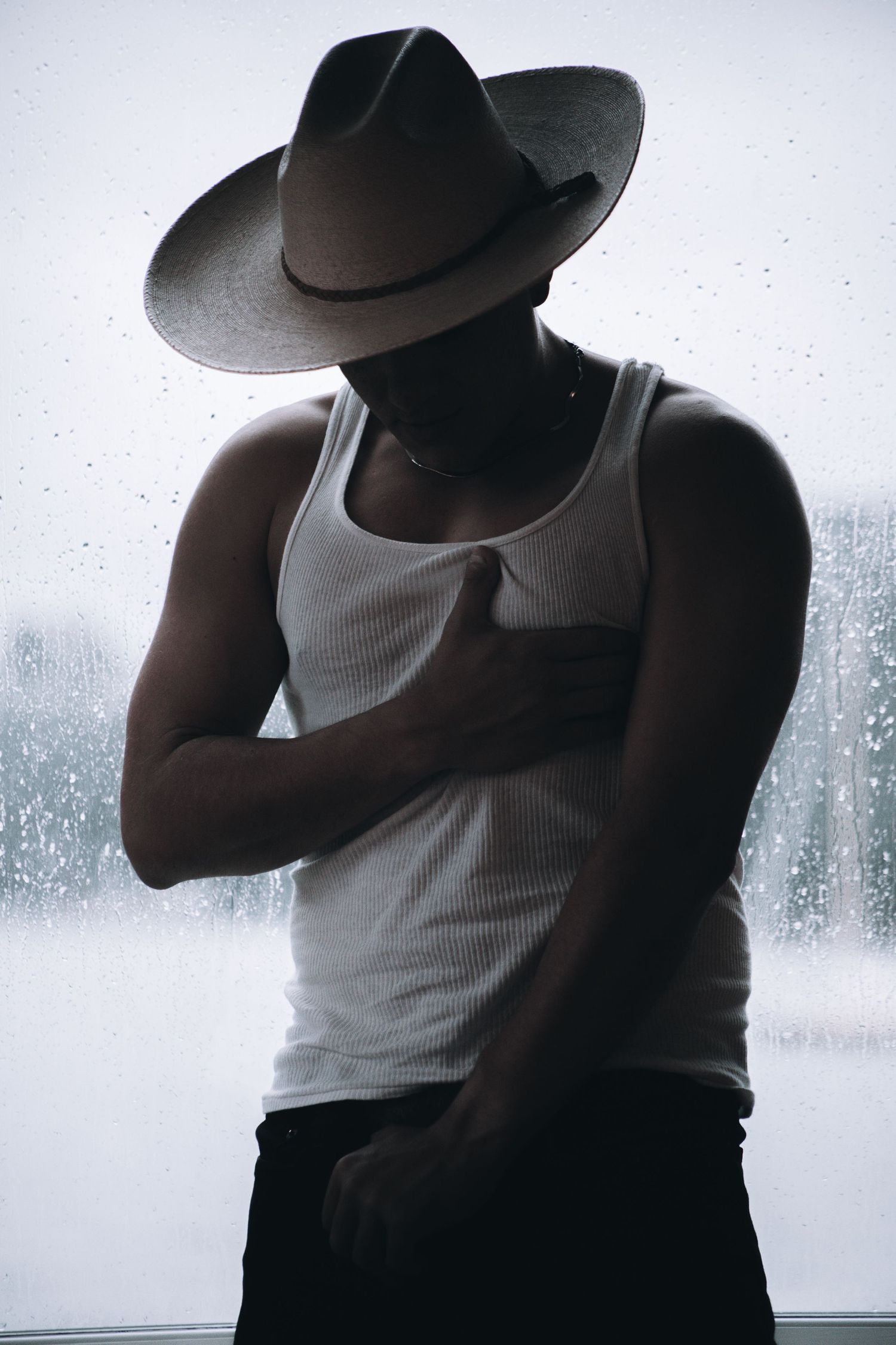 Stylized photos of person in white tank top and hat creating film noir aesthetic against rainy window.
