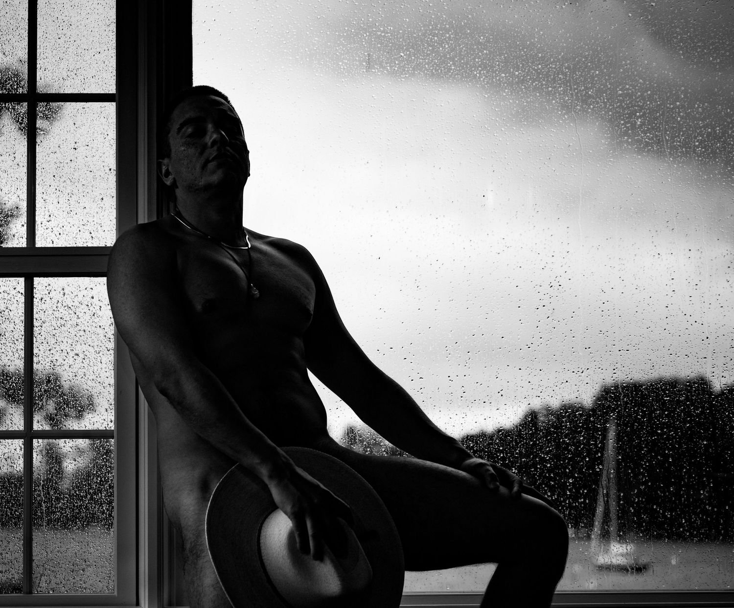 Artistic silhouette of a person seated by a window on a rainy day.