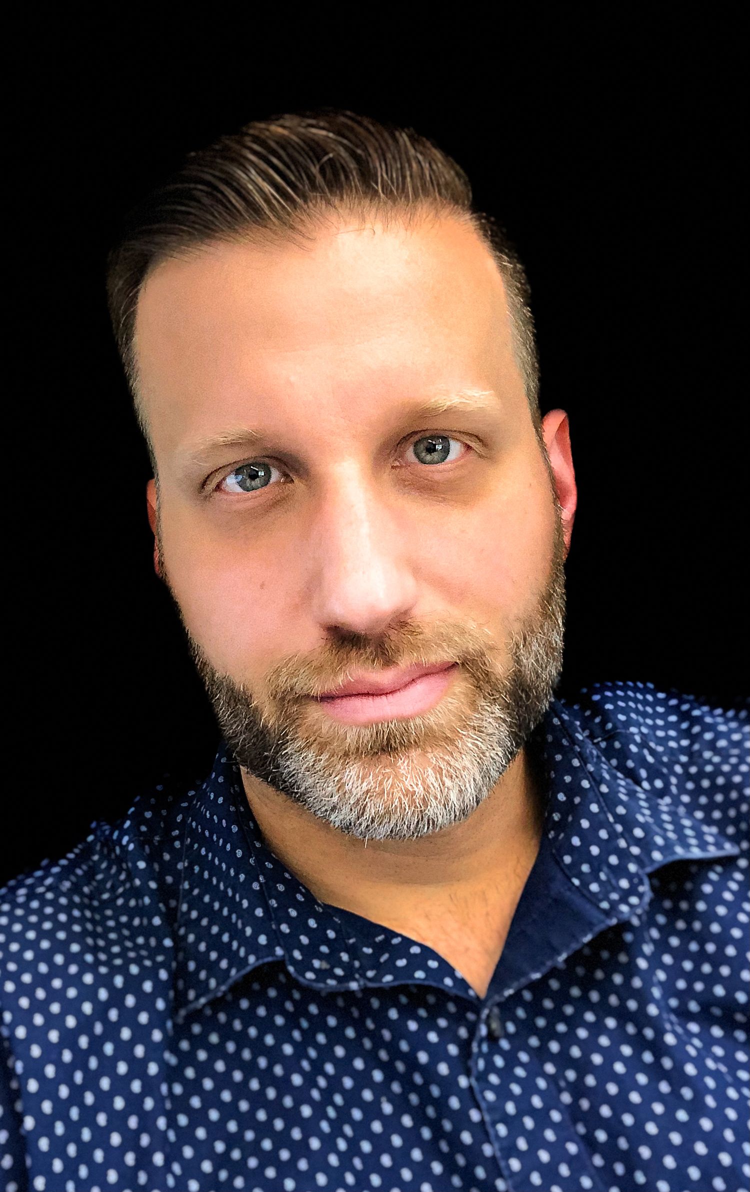 Portrait in polka dot navy shirt against dark background.