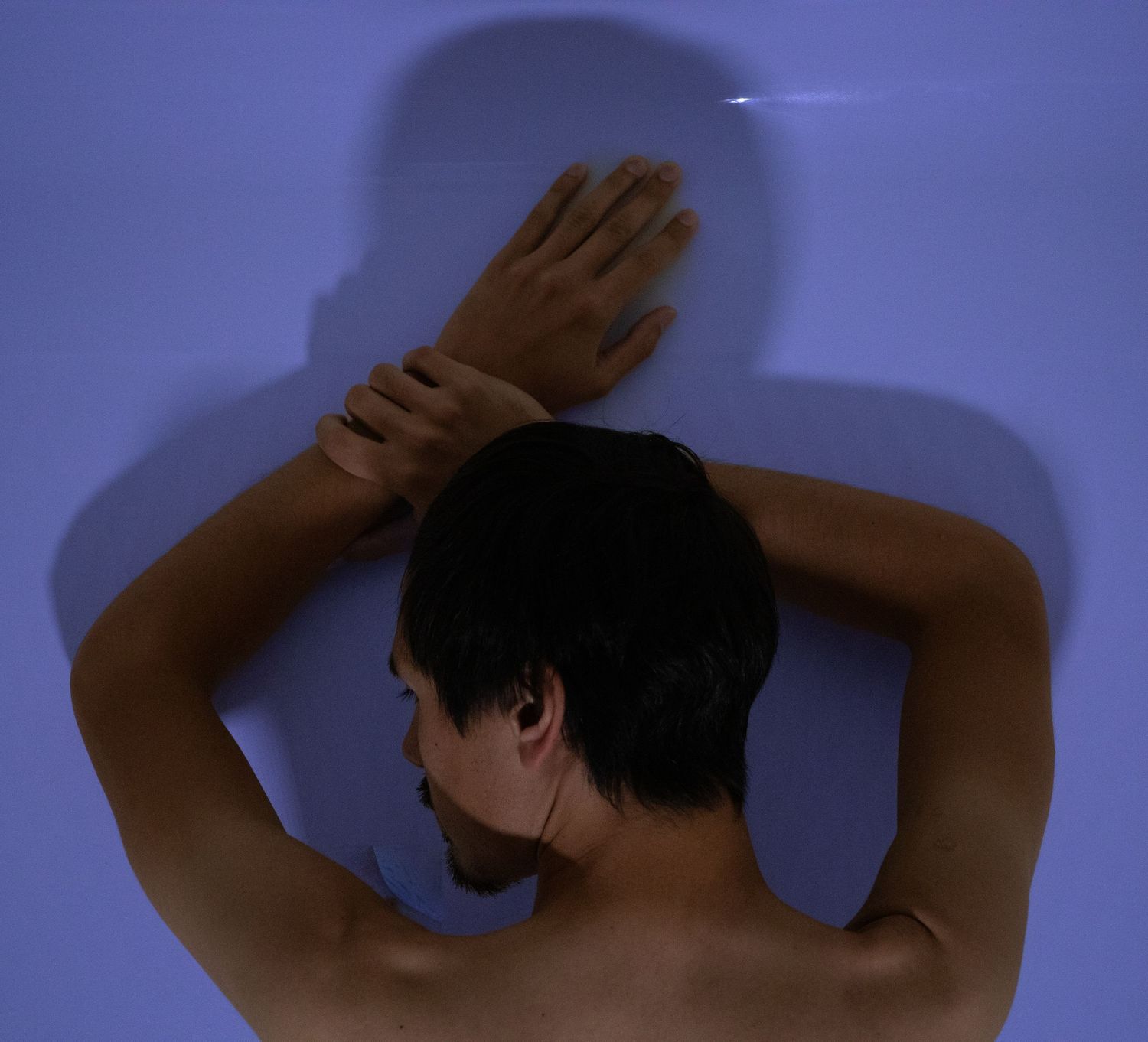 Abstract artistic nude study with blue lighting and raised arms.